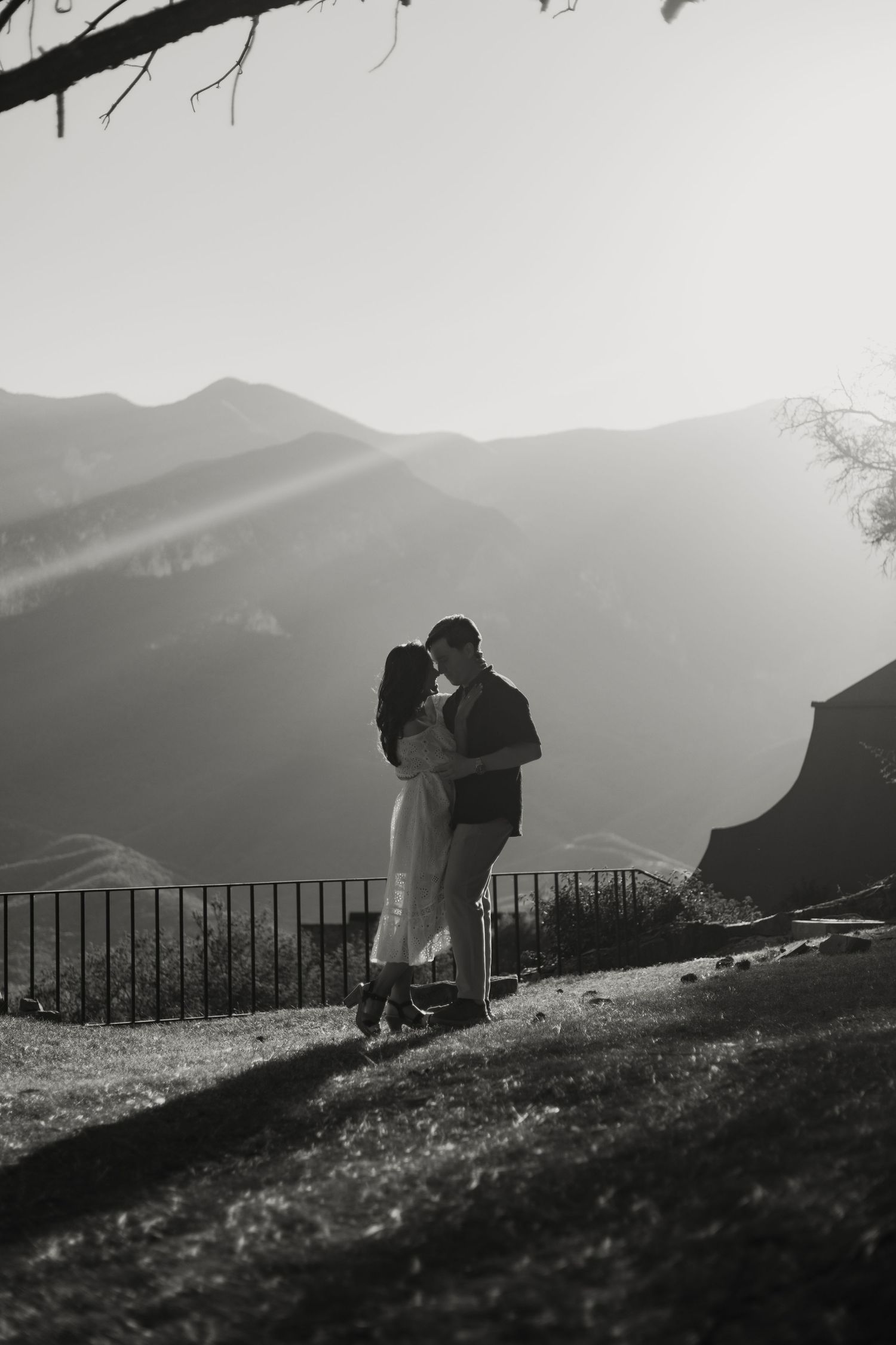 Black and white romantic photo of a couple embracing with stunning mountain landscape behind them.