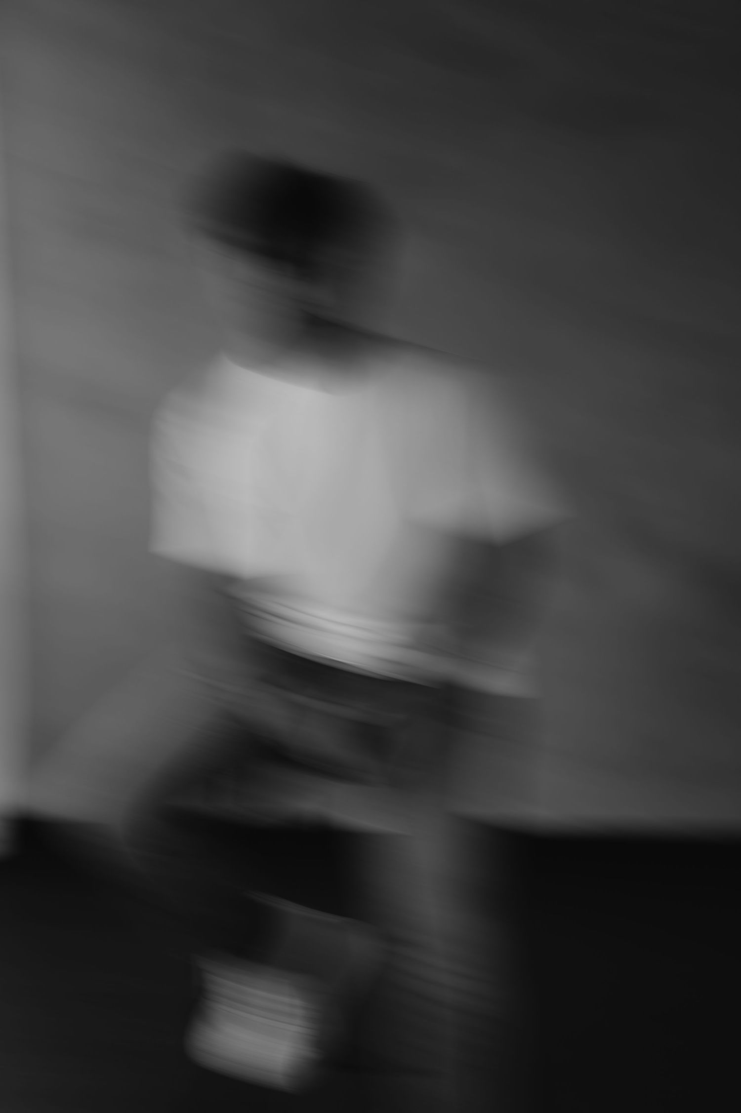 Blurry black and white photo of a person in motion wearing a white t-shirt, creating an abstract artistic effect.