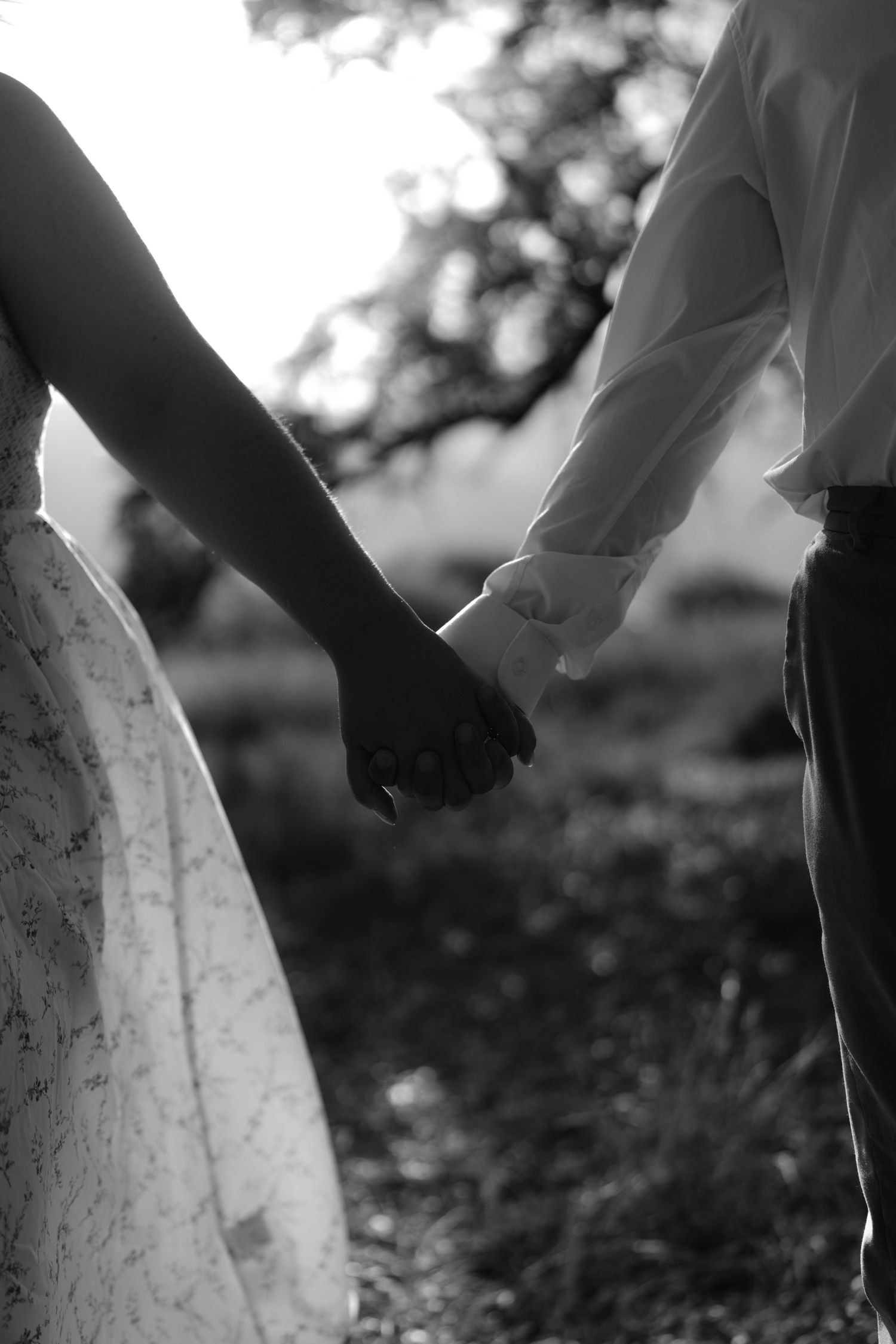 Black and white photo of a bride and groom holding hands outdoors, symbolizing love and unity on their wedding day.