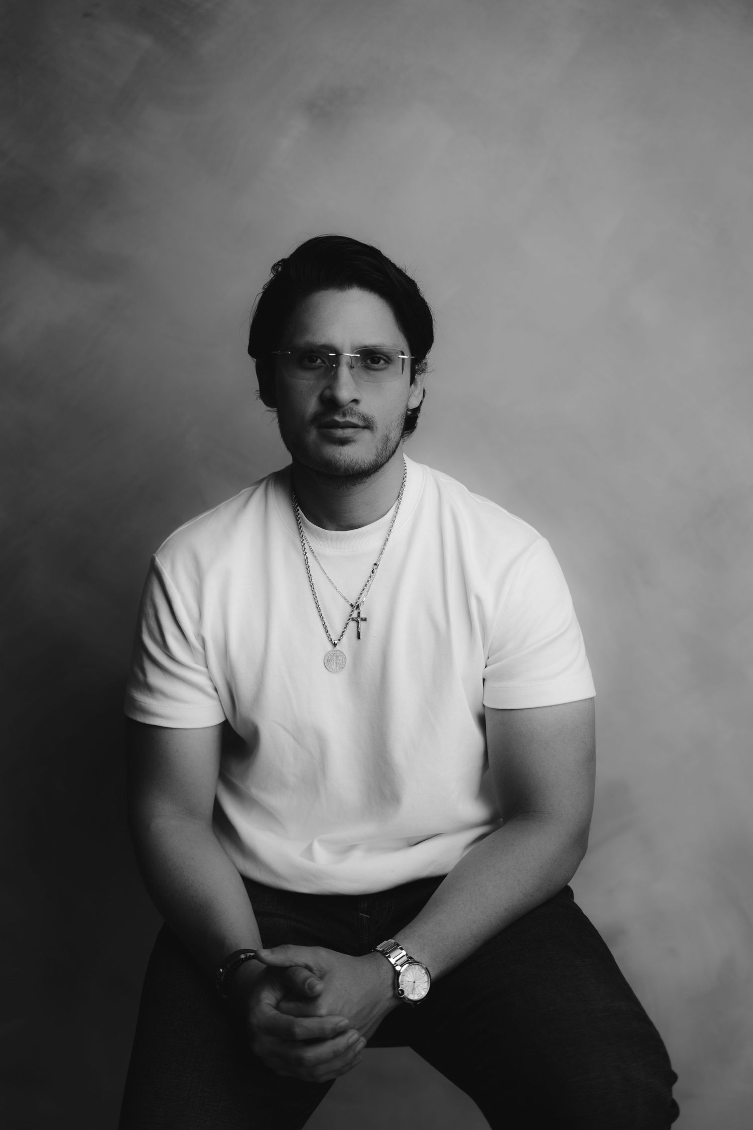 Young man in white t-shirt and cross necklace poses confidently in a classic black and white studio portrait.