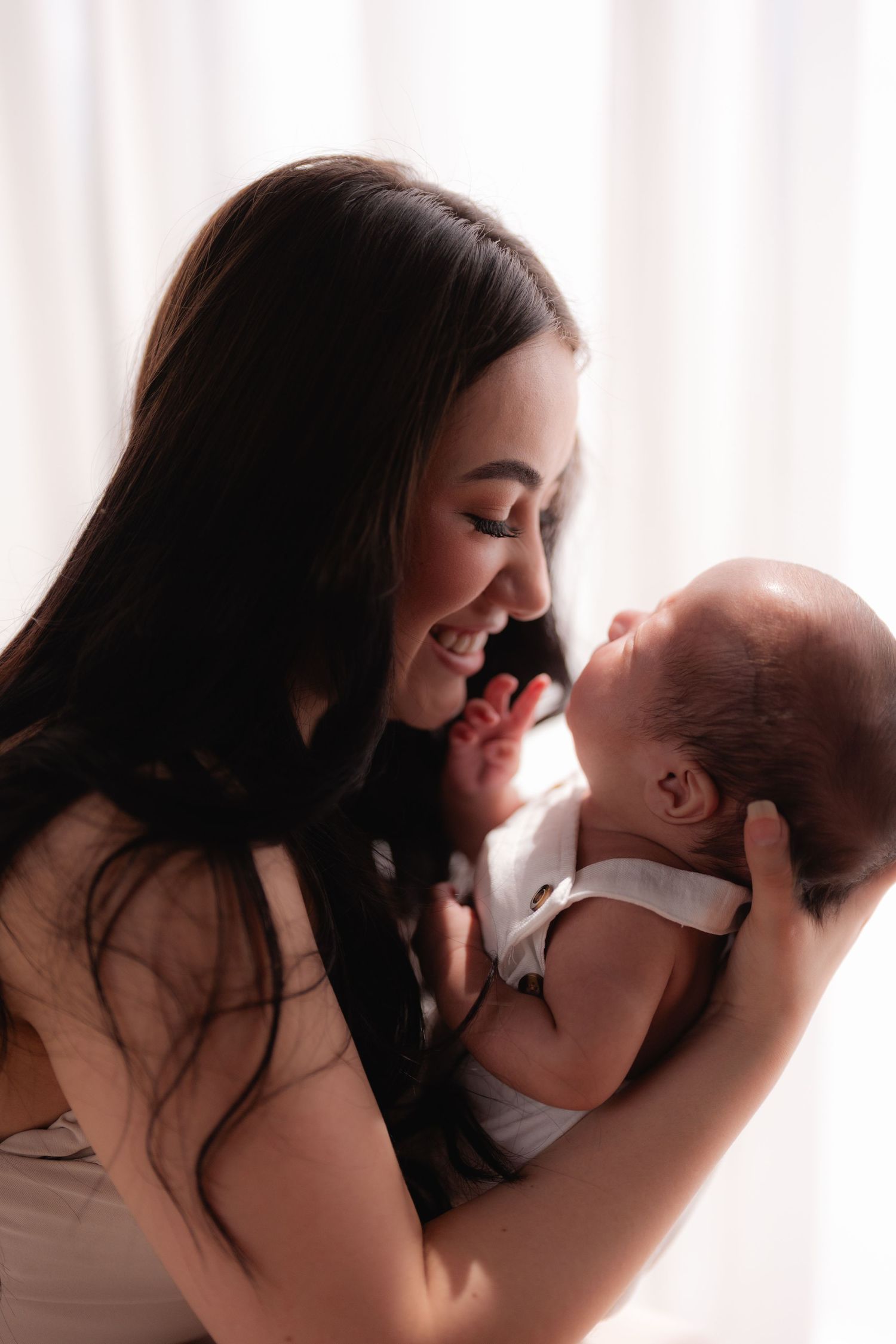 A smiling young mother with dark hair gently holds her newborn baby close, sharing a tender moment.
