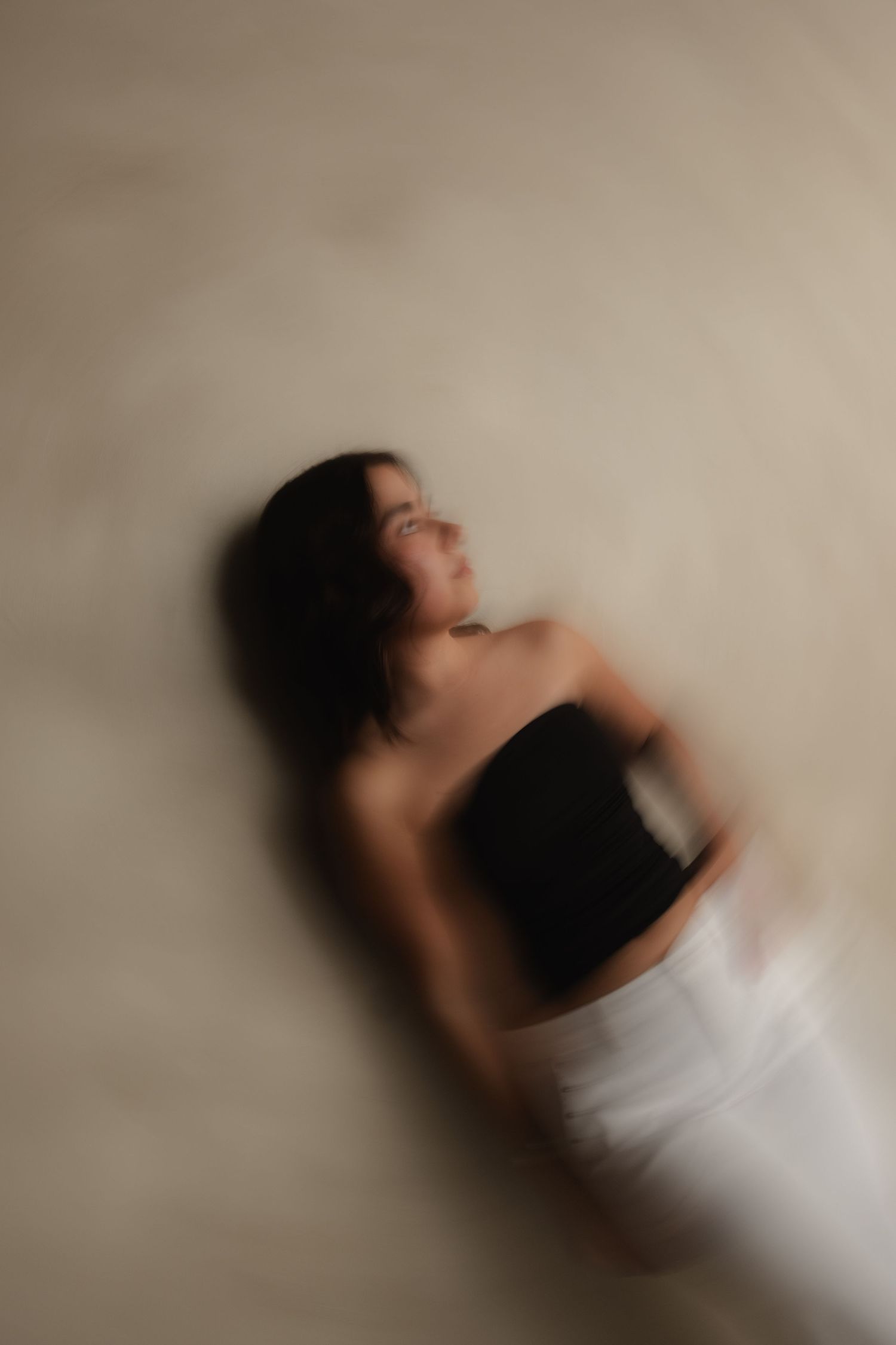 Artistic blurred motion portrait of a woman in a black top and white skirt against a neutral background.