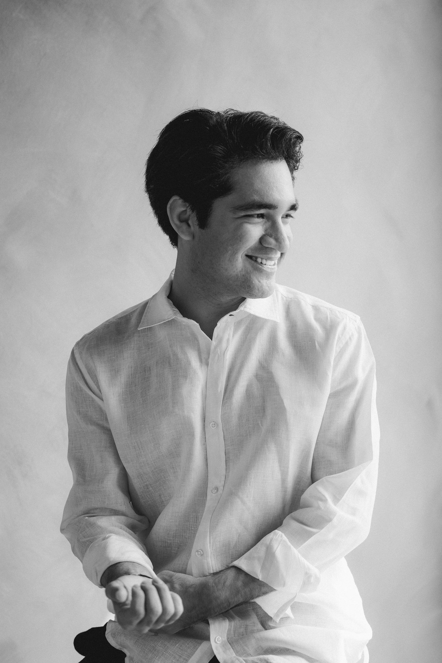 Smiling young man in white linen shirt poses in classic black and white studio portrait.