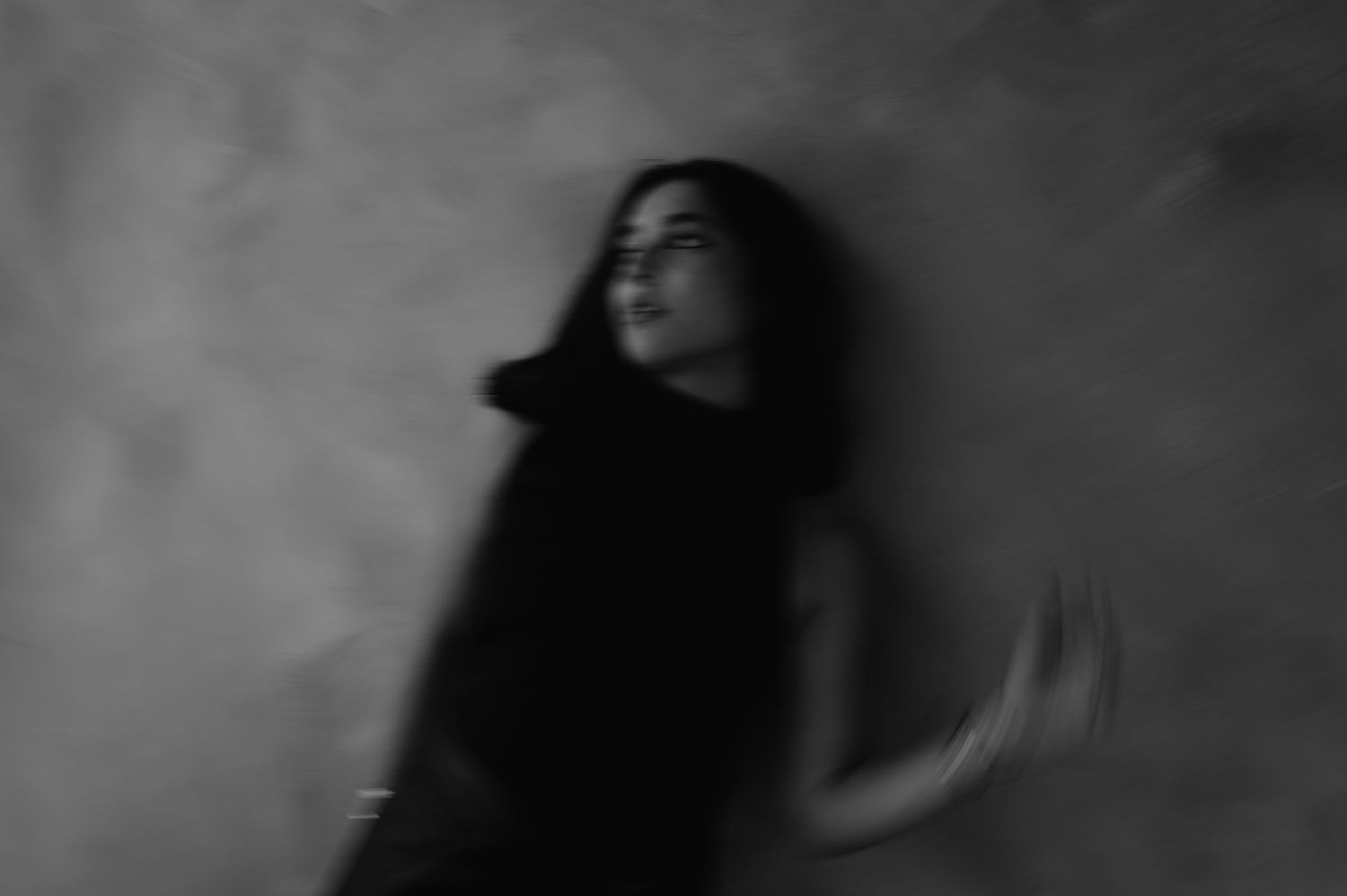 Artistic blurred black and white portrait of a woman in motion against a textured wall background.