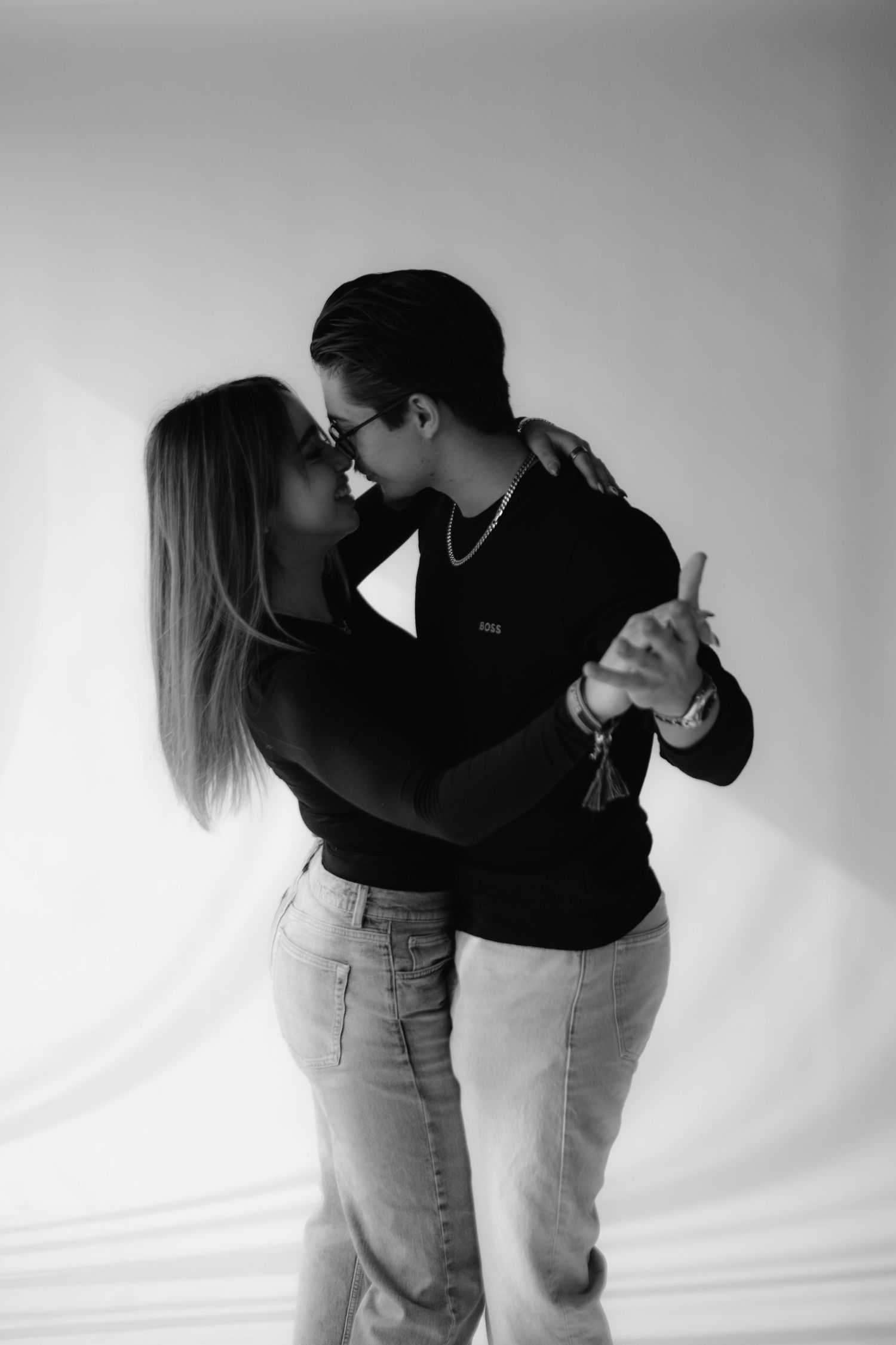 Black and white photo of a couple kissing and dancing together against a soft light background.