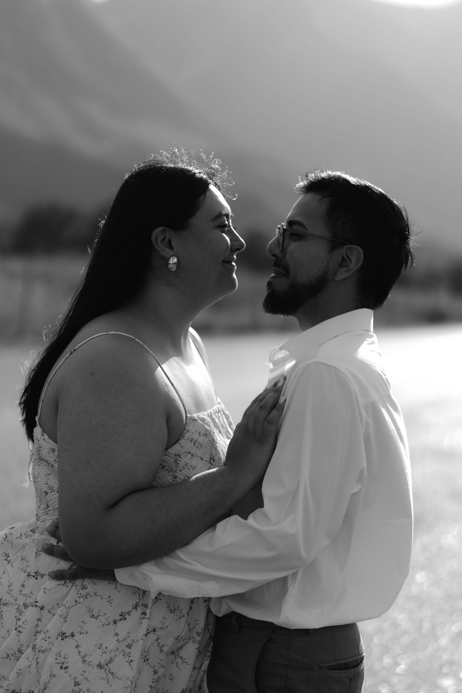 Black and white photo of a couple sharing a romantic moment outdoors with mountains in the background.