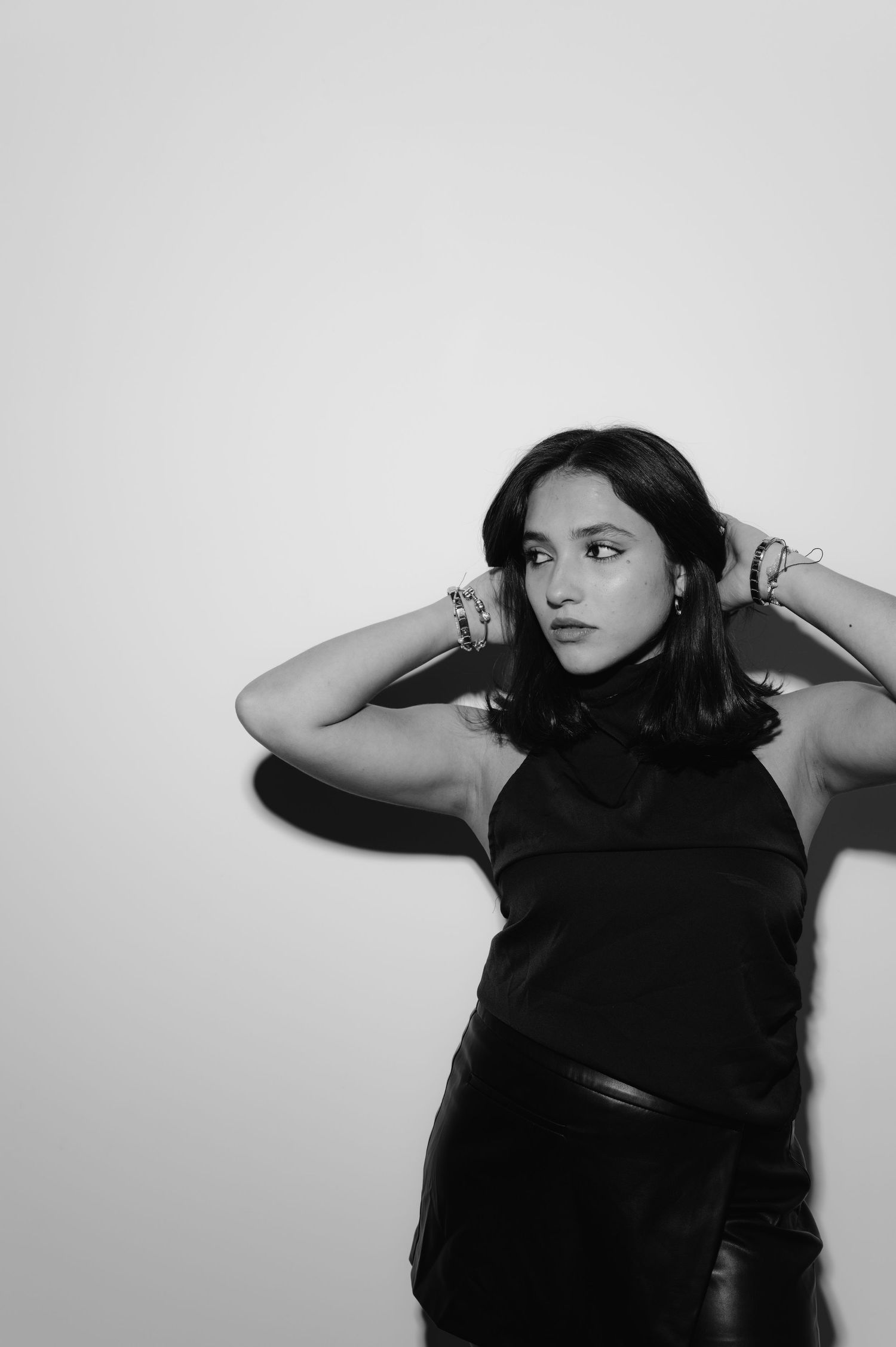 Black and white portrait of a young woman in a black top posing with hands behind her head.