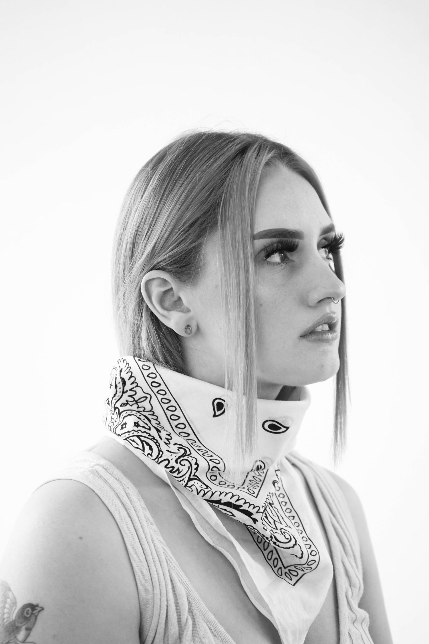 Black and white image of girl on white backdrop looking away from camera with white bandana on her neck