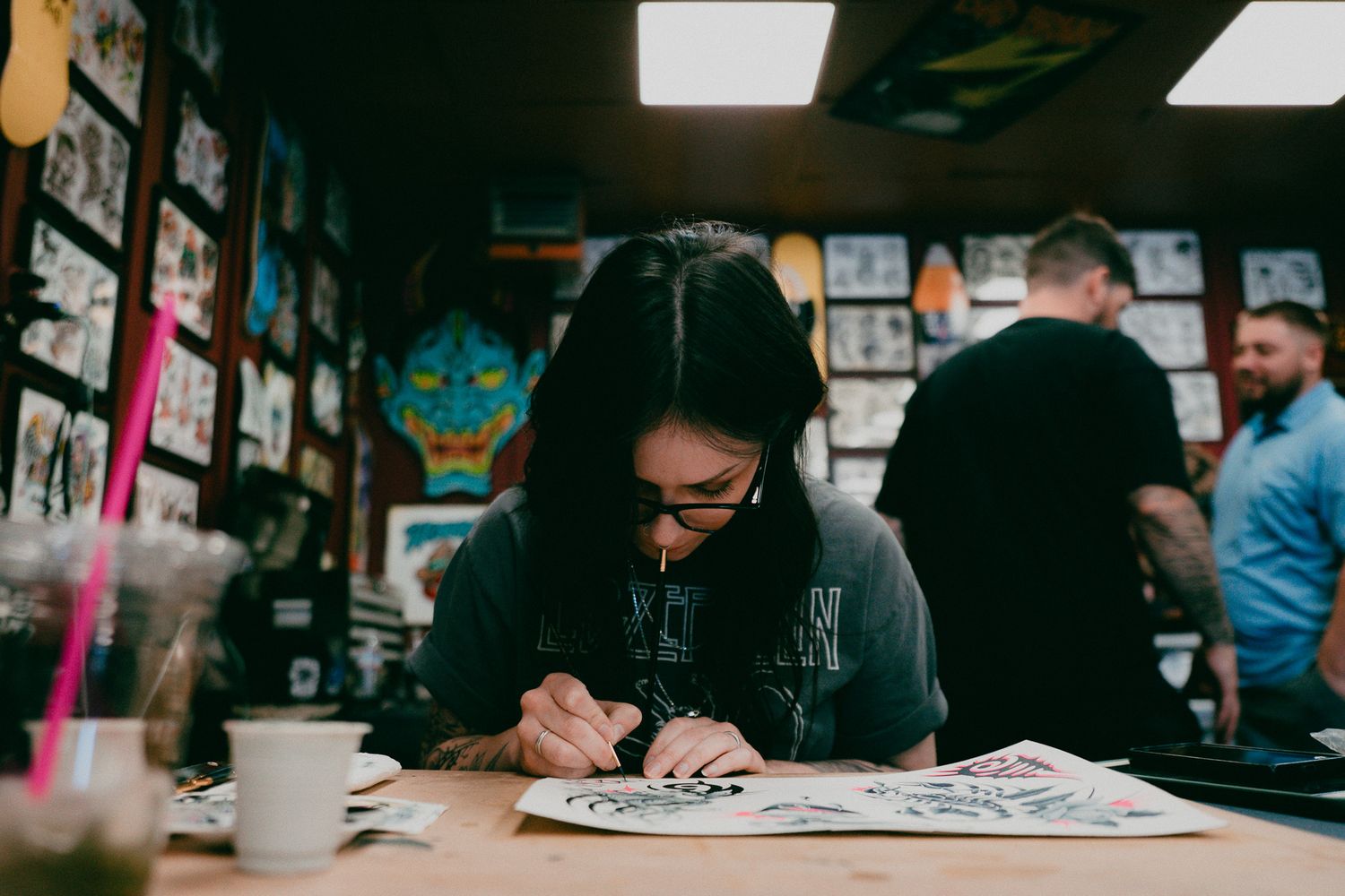 A female tattoo artist practicing her art, looking down at paper with a paintbrush in her mouth
