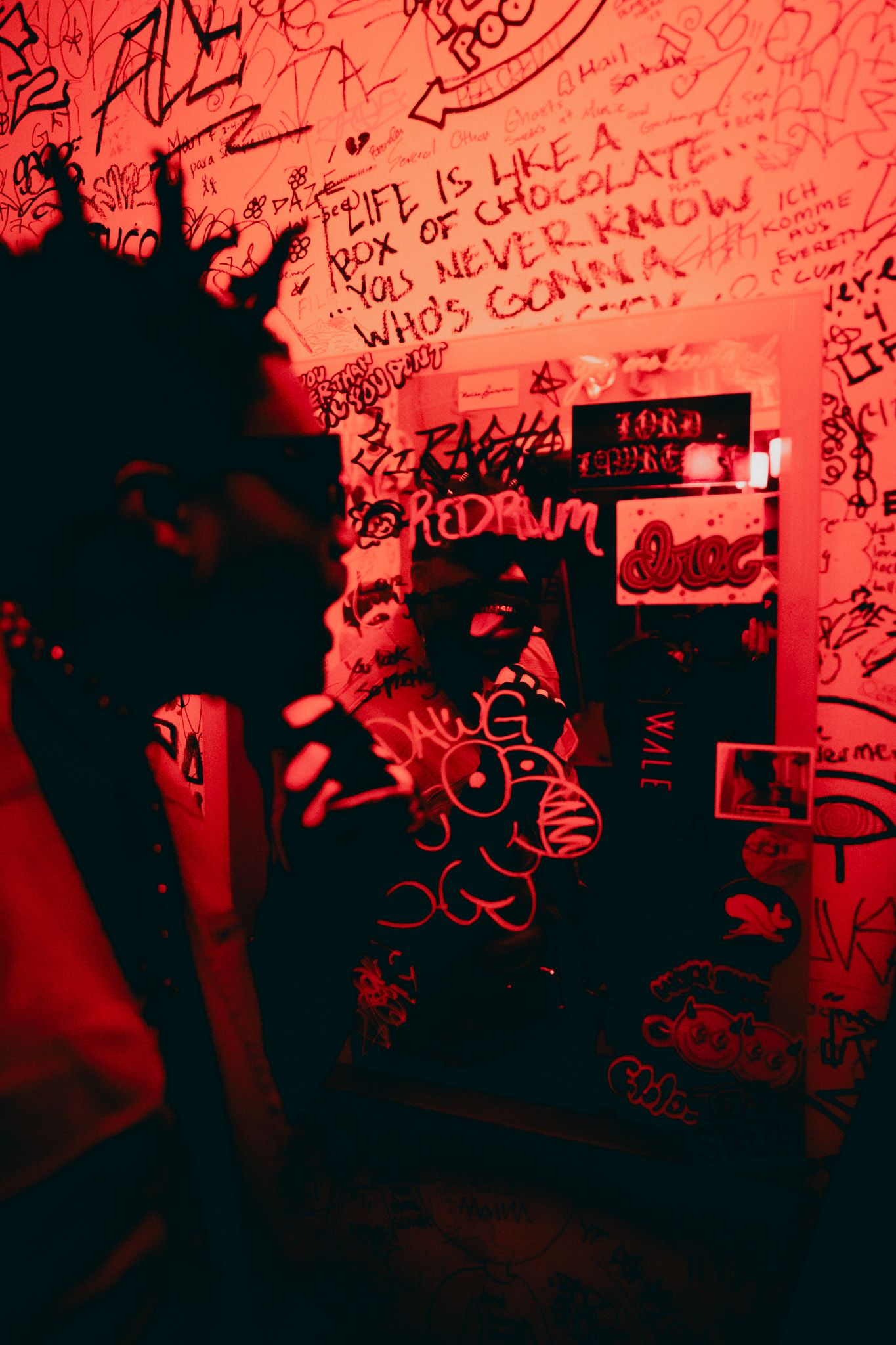 Man looking in a mirror covered in graffiti, sticking his tongue out at himself