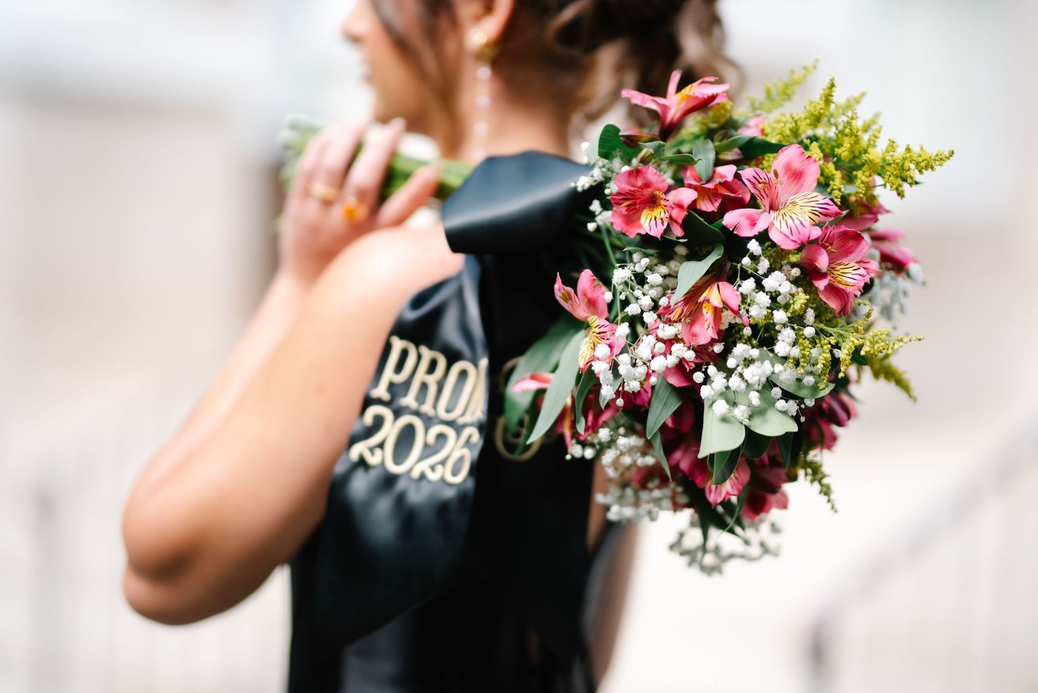 A prom 2023 student holds a vibrant bouquet of pink lilies, baby's breath, and greenery at a prom event.