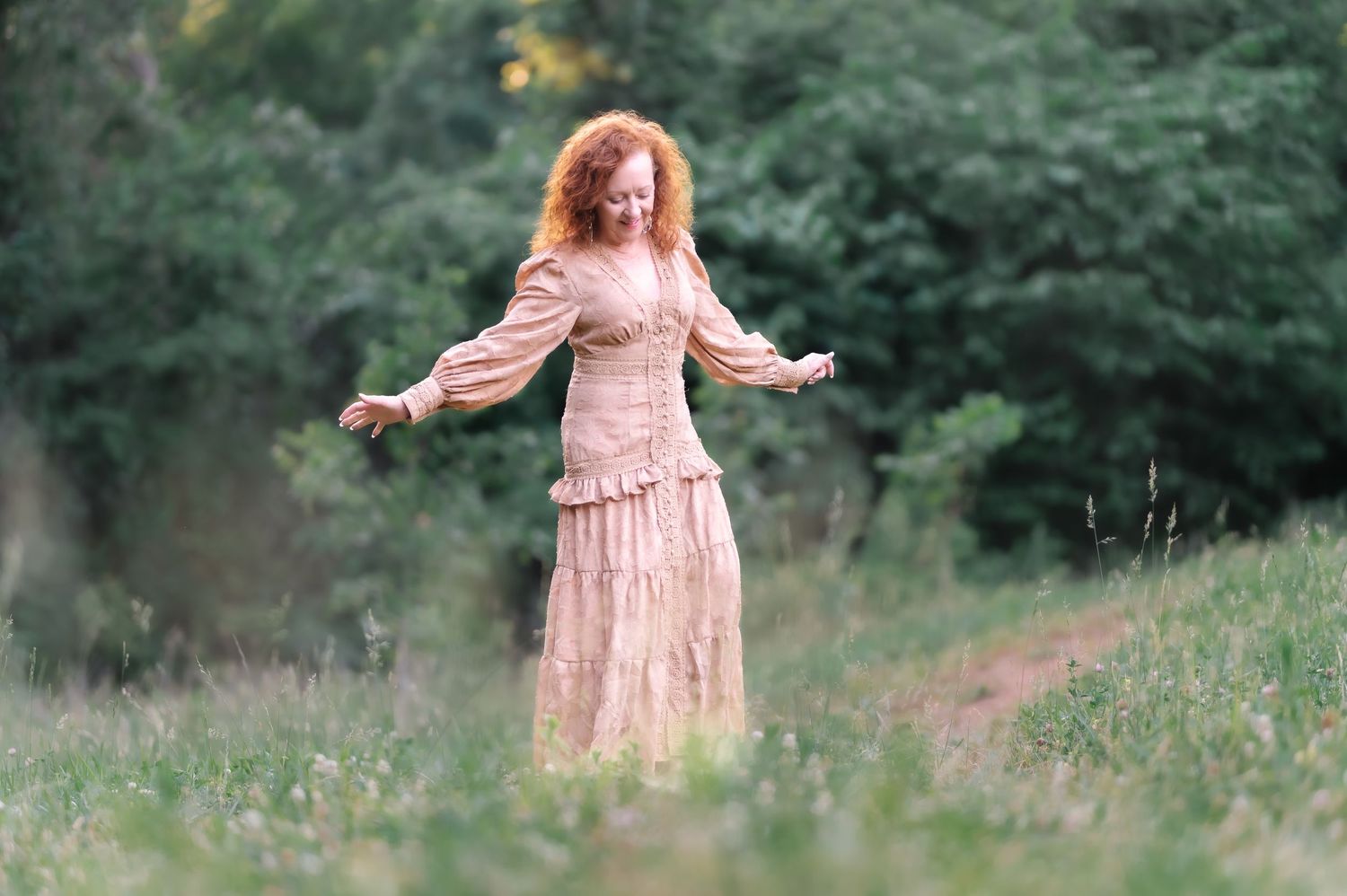 A woman with curly red hair twirls in a vintage pink dress in a lush green meadow.