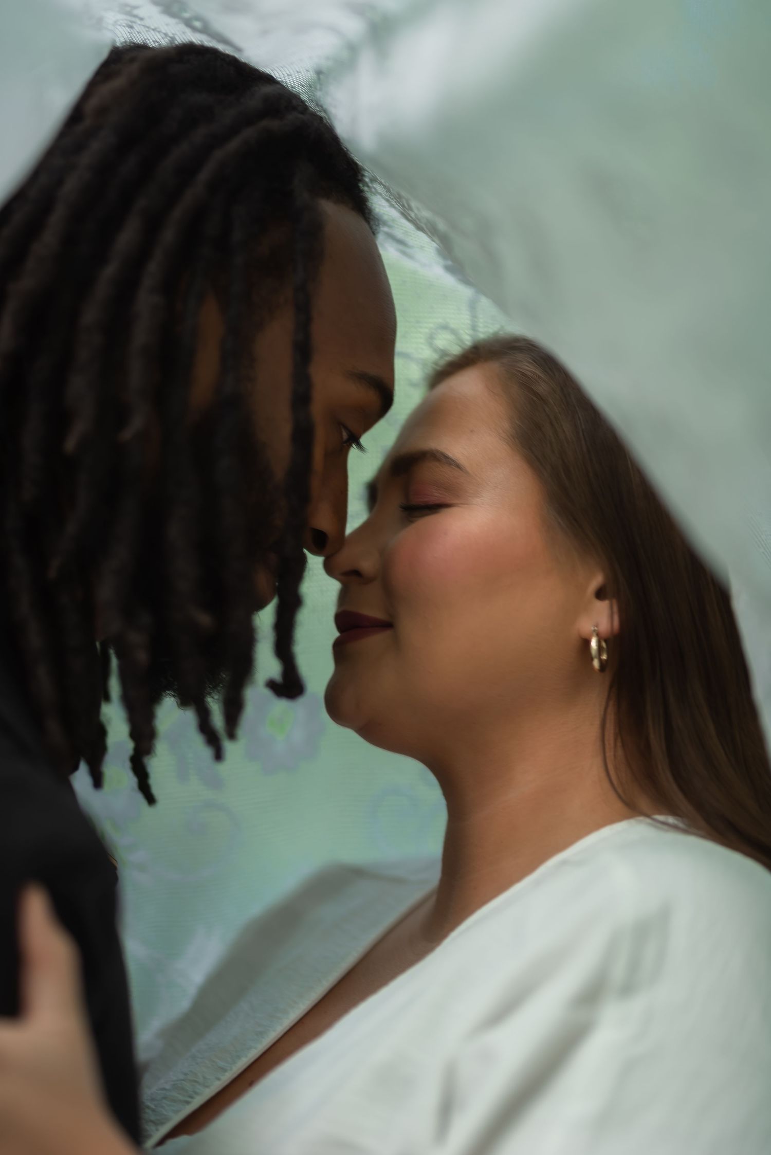 A romantic interracial couple sharing an intimate moment, nearly kissing, with the woman wearing a white robe and gold earrings.