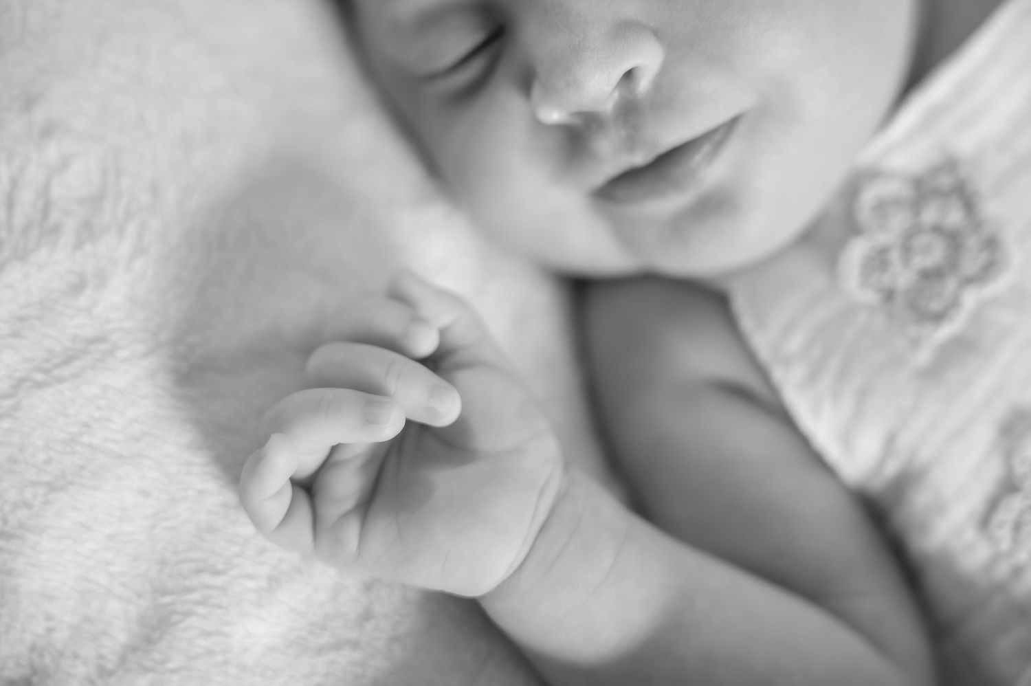 Black and white close-up of a sleeping newborn baby with tiny curled fingers resting on a soft white blanket.