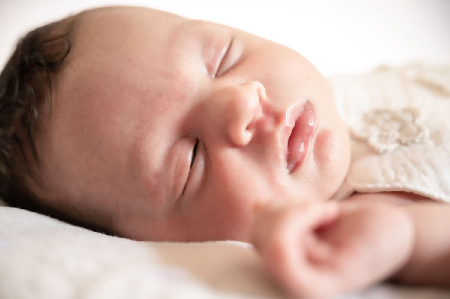 Peaceful newborn baby sleeping soundly, with delicate features and soft skin, wearing a white lace outfit.