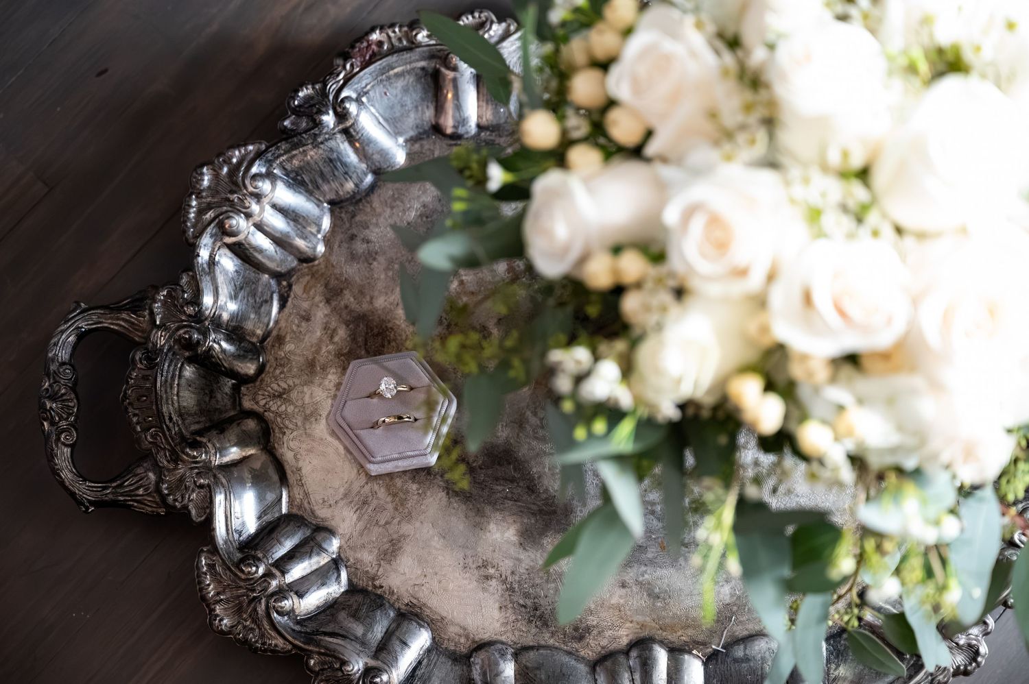 Elegant silver tray with a hexagonal ring box and white roses bouquet, perfect for a wedding flat lay display.
