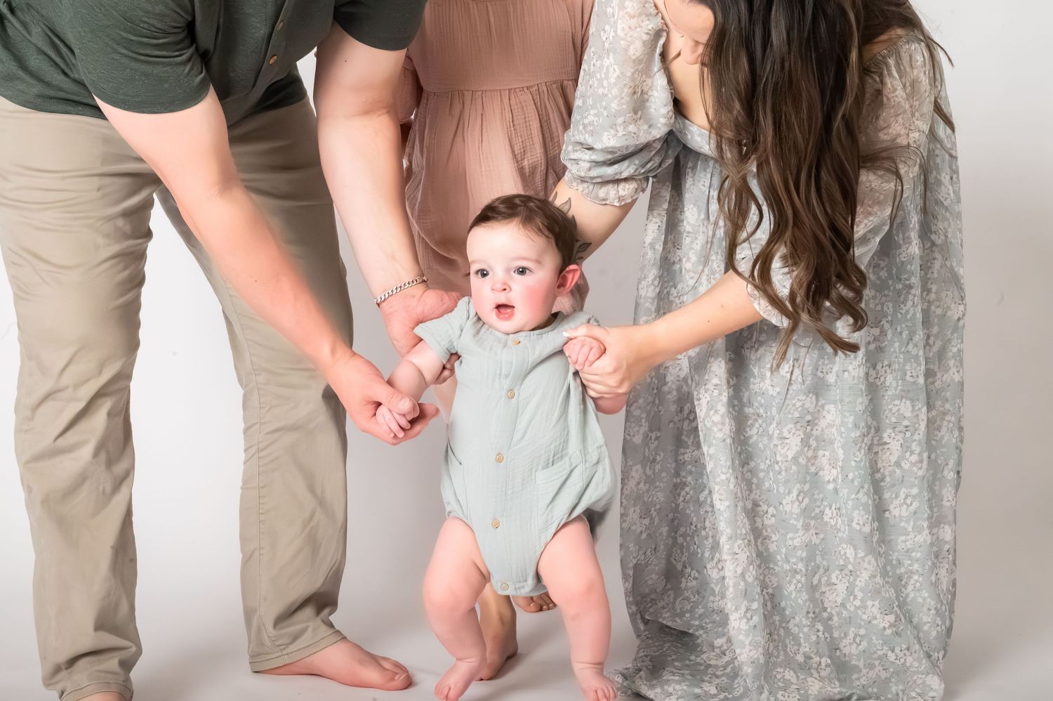 Parents helping their baby take first steps in a studio portrait session with neutral tones.