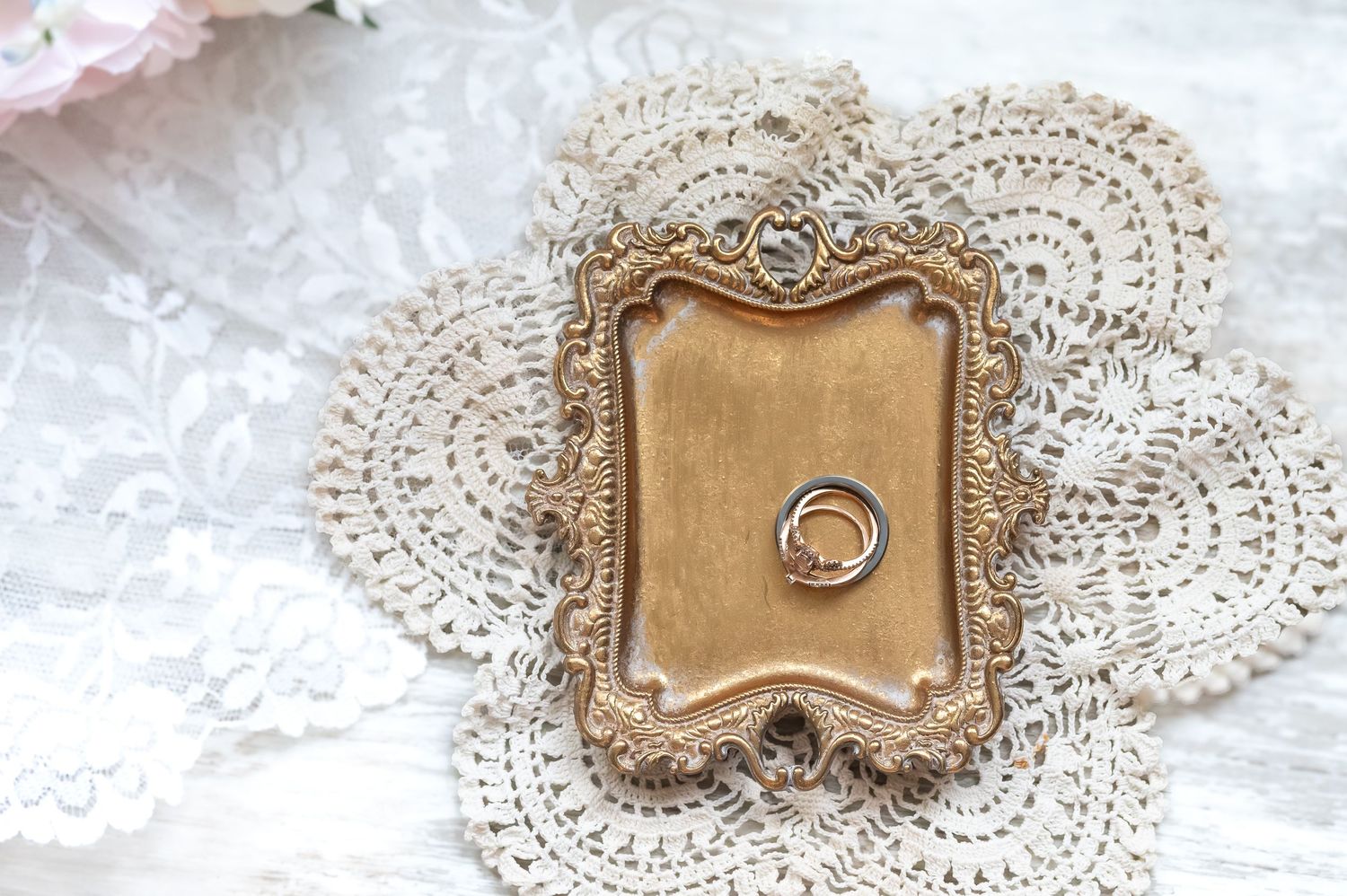 Gold ornate frame with wedding rings on a lace doily, elegant vintage bridal ring bearer display.