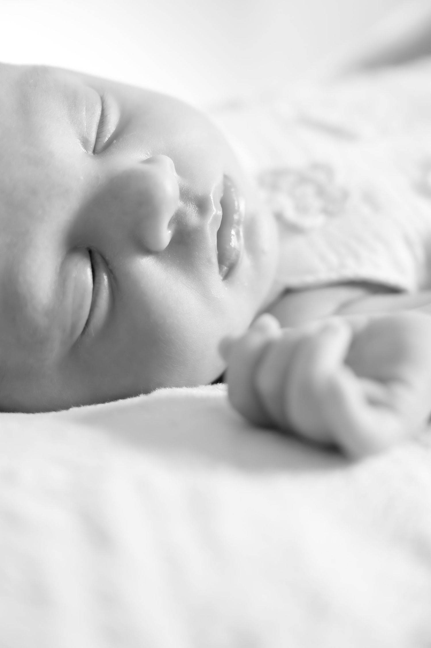 Black and white photo of a peaceful sleeping newborn baby lying on a soft white blanket.