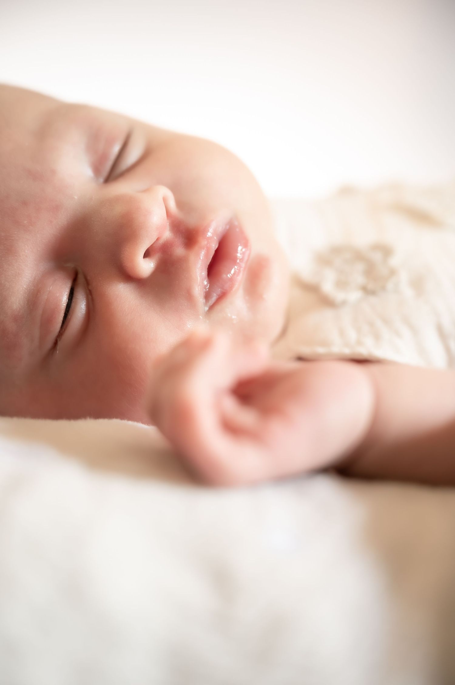 Close-up of a peaceful sleeping newborn baby resting on a soft white fluffy blanket.