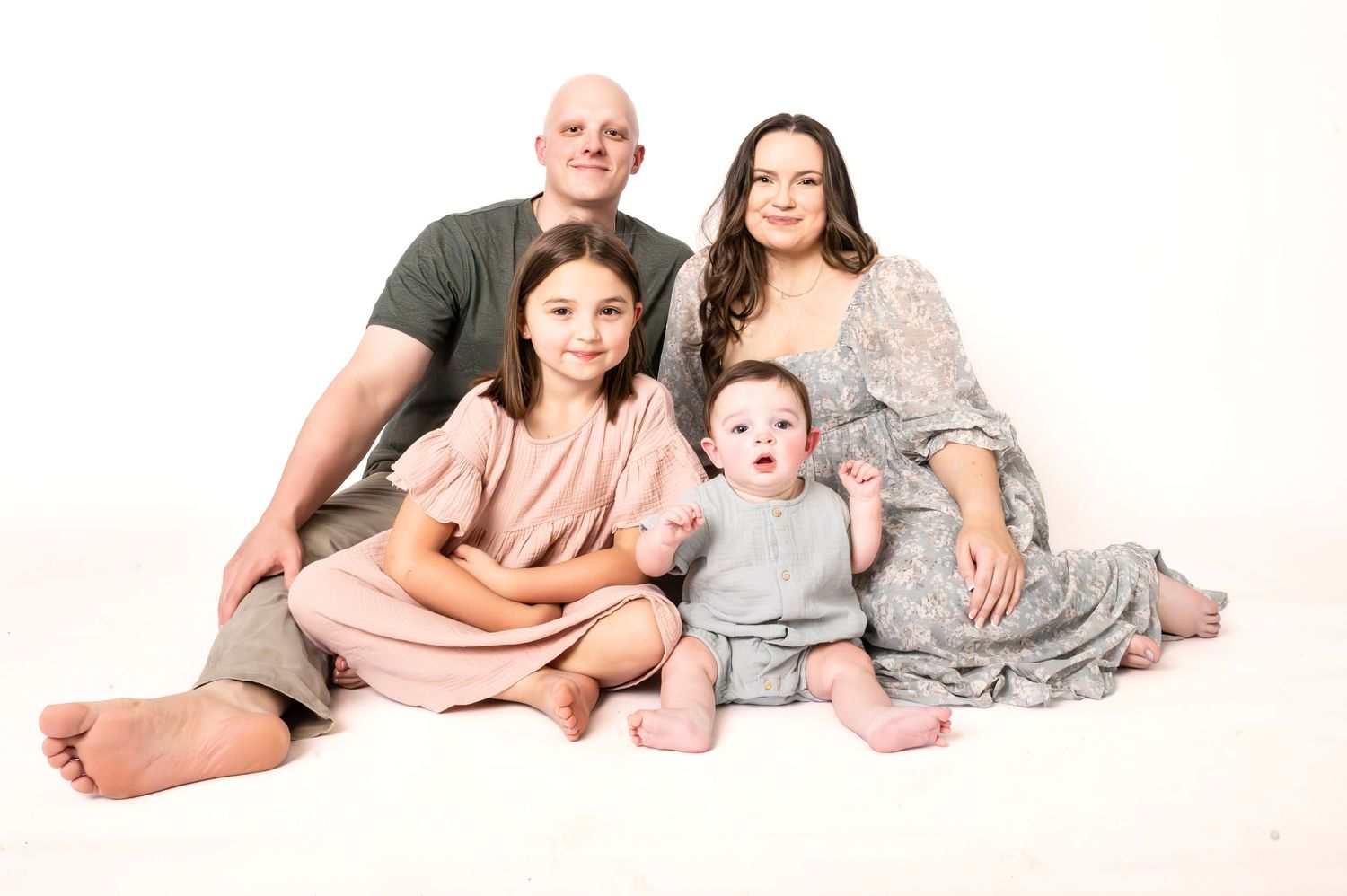 Family of four posing for a professional studio portrait on white background, including parents and two young children.
