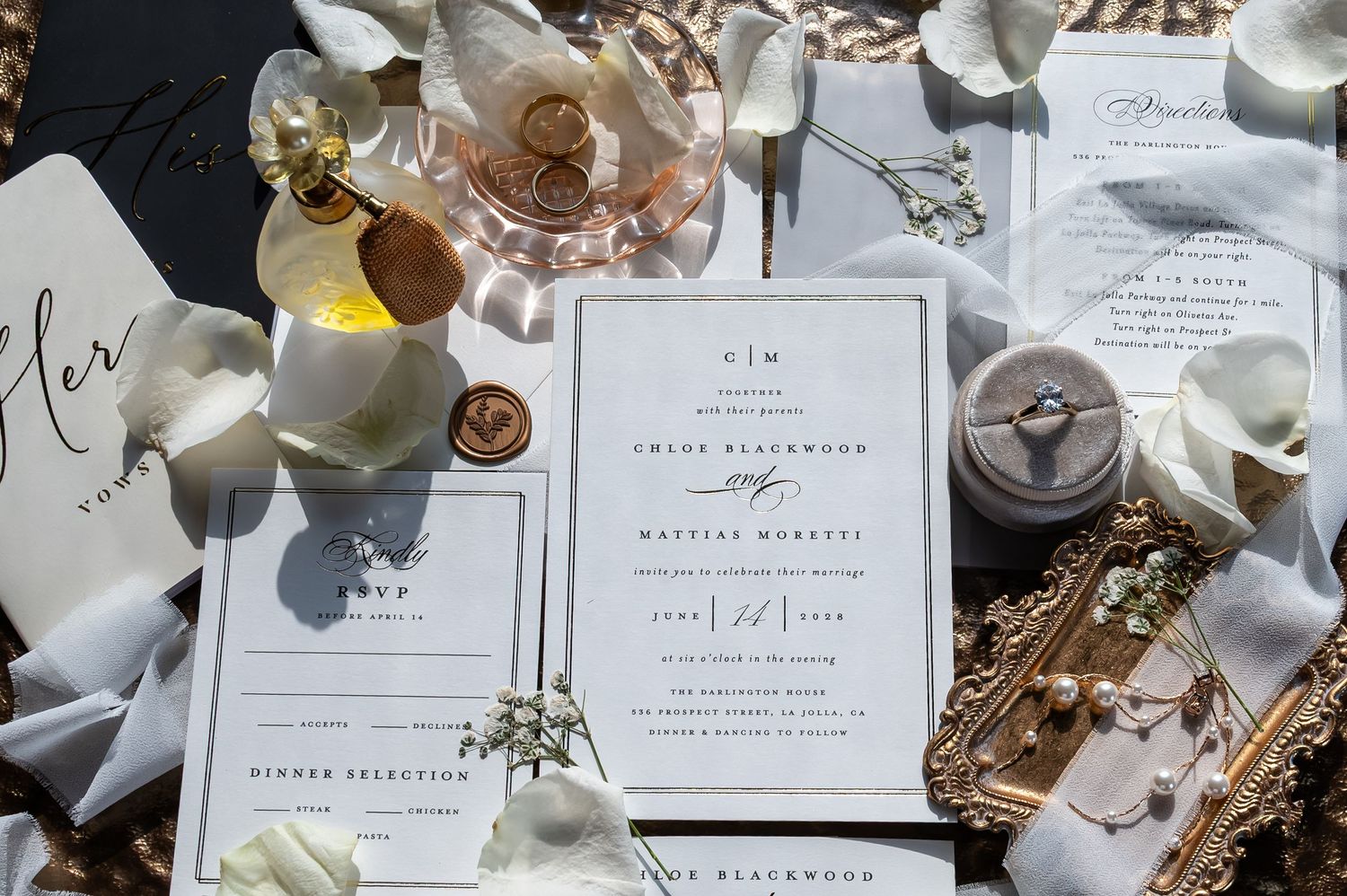 Elegant wedding invitation suite with wax seal, ring box, floral accents, and rose gold details on a dark background.