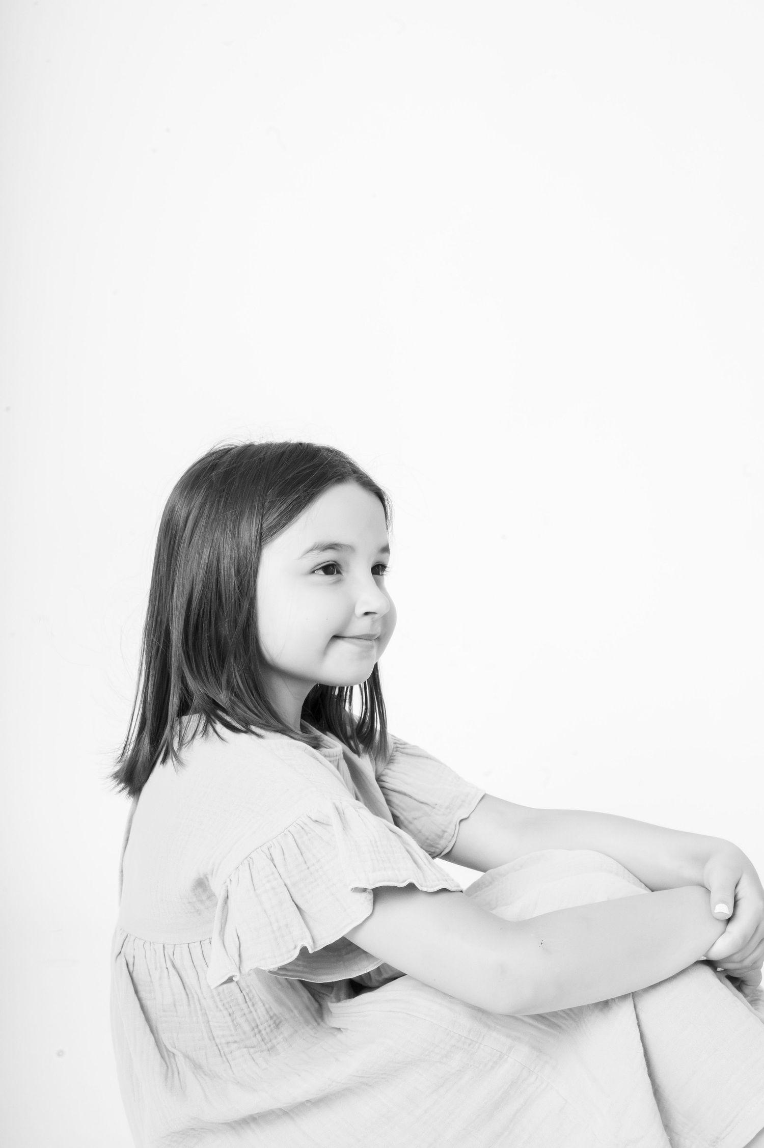 Black and white portrait of a young girl with shoulder-length hair sitting and smiling against a white background.