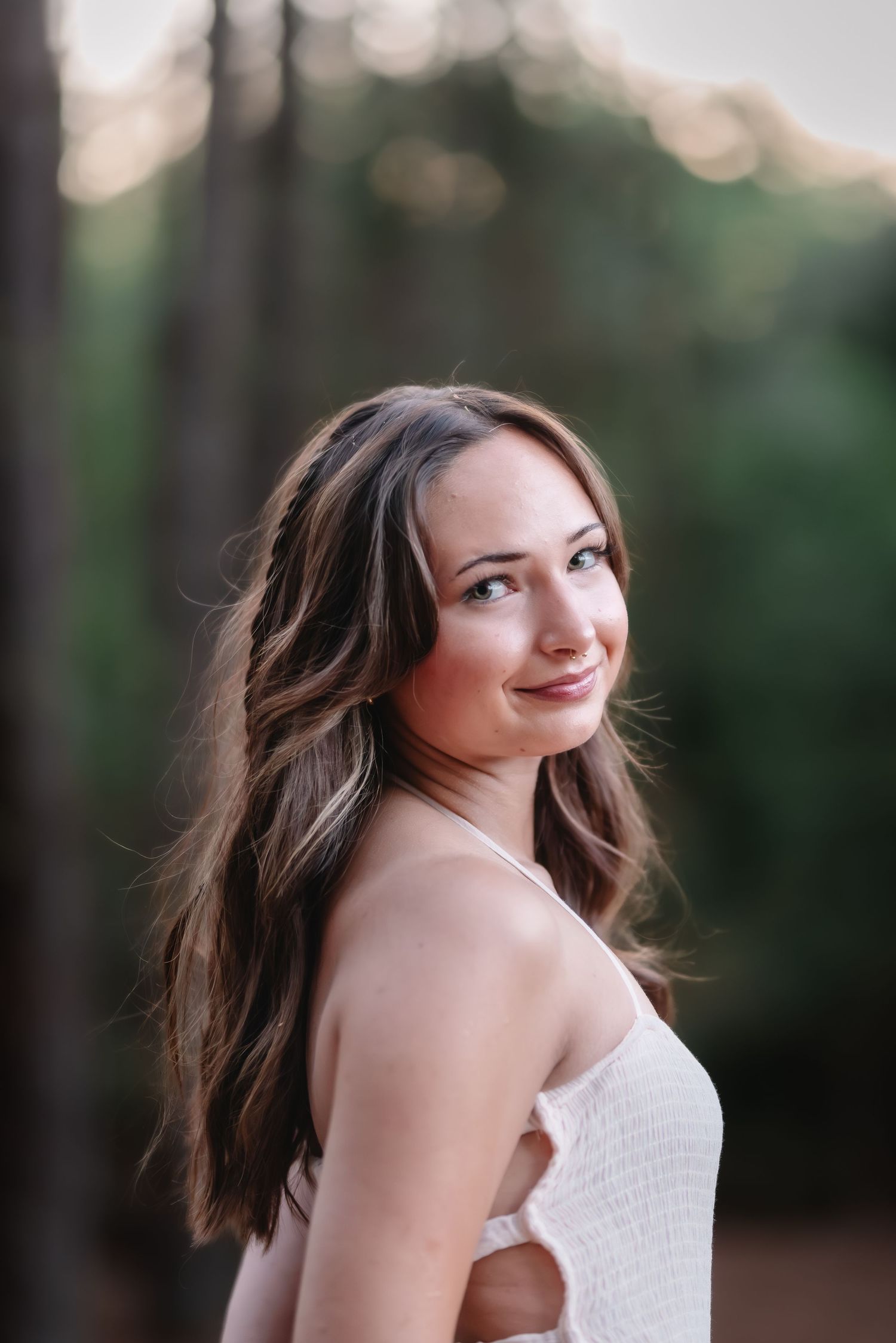 Young woman with long brown hair smiling over her shoulder outdoors in soft natural light.