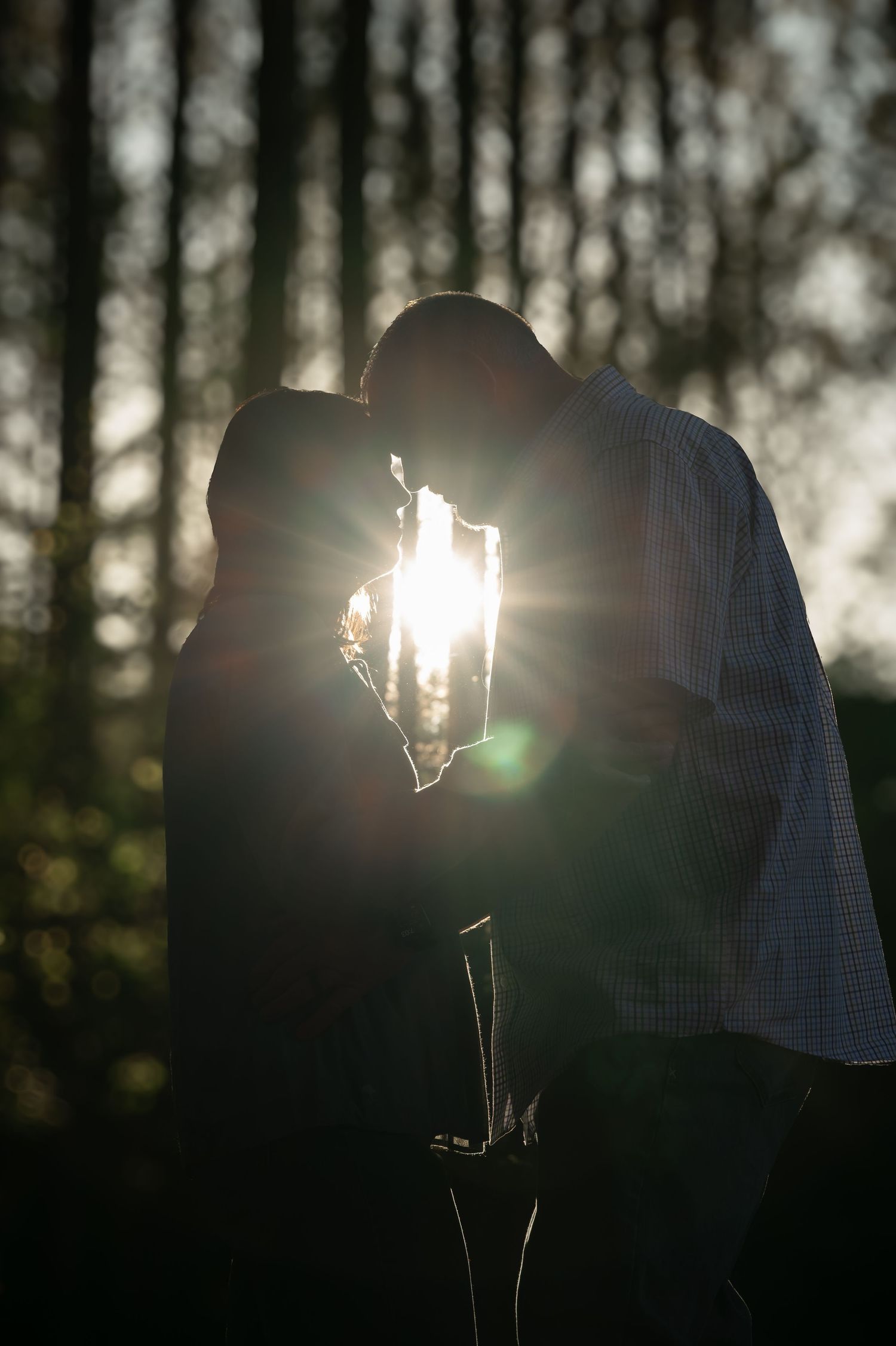 Silhouette of a couple sharing a romantic moment at sunset in a forest, with sunlight glowing between them.