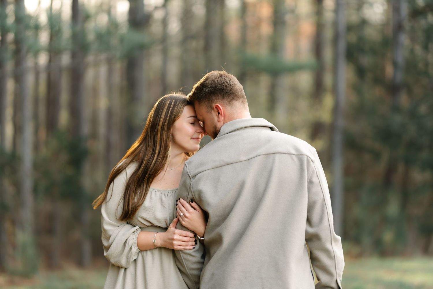 A romantic couple embraces tenderly in a misty pine forest, dressed in matching gray outfits.