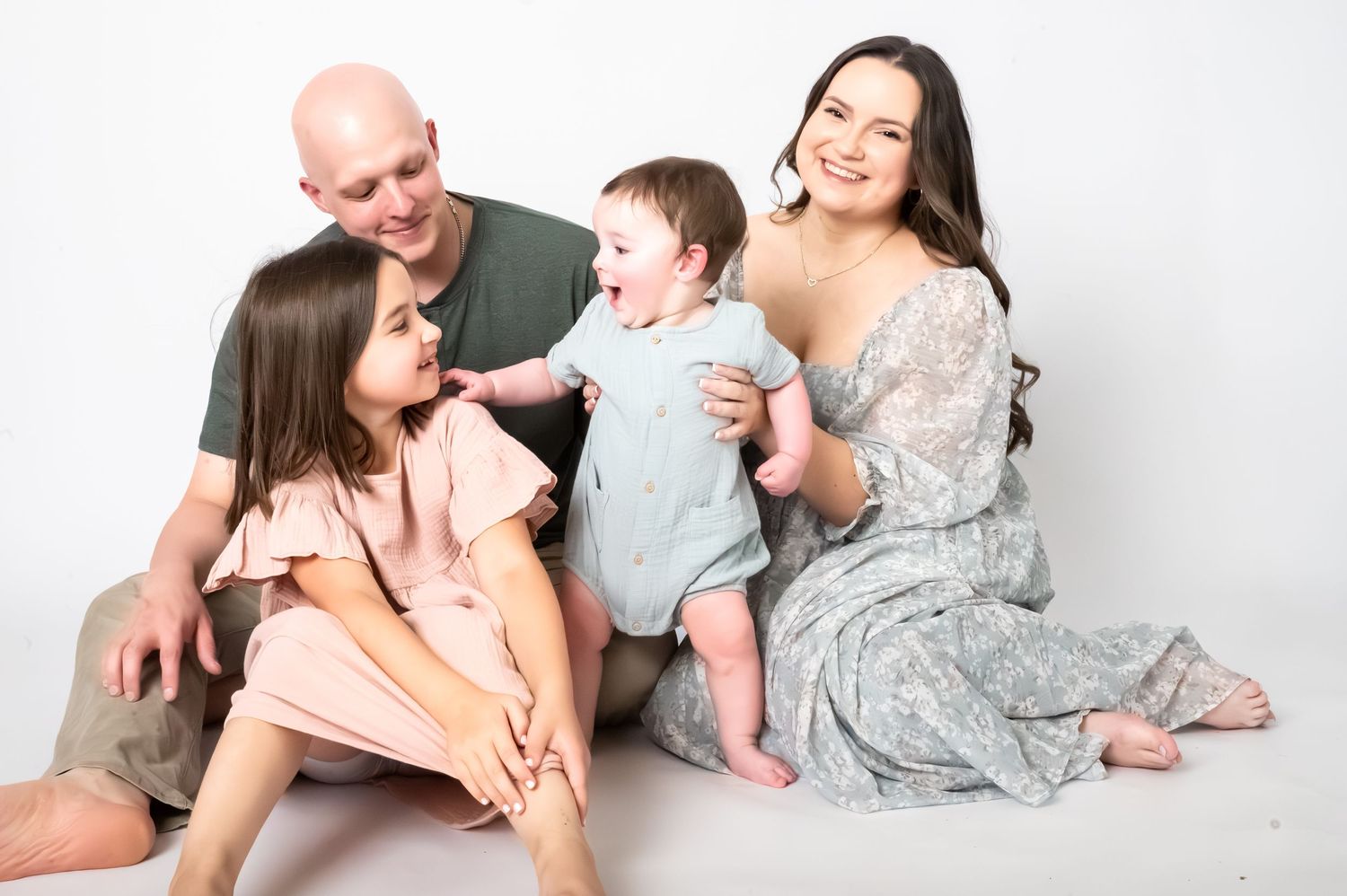 Happy family of four posing together on white background, parents with young daughter and baby boy in studio portrait.