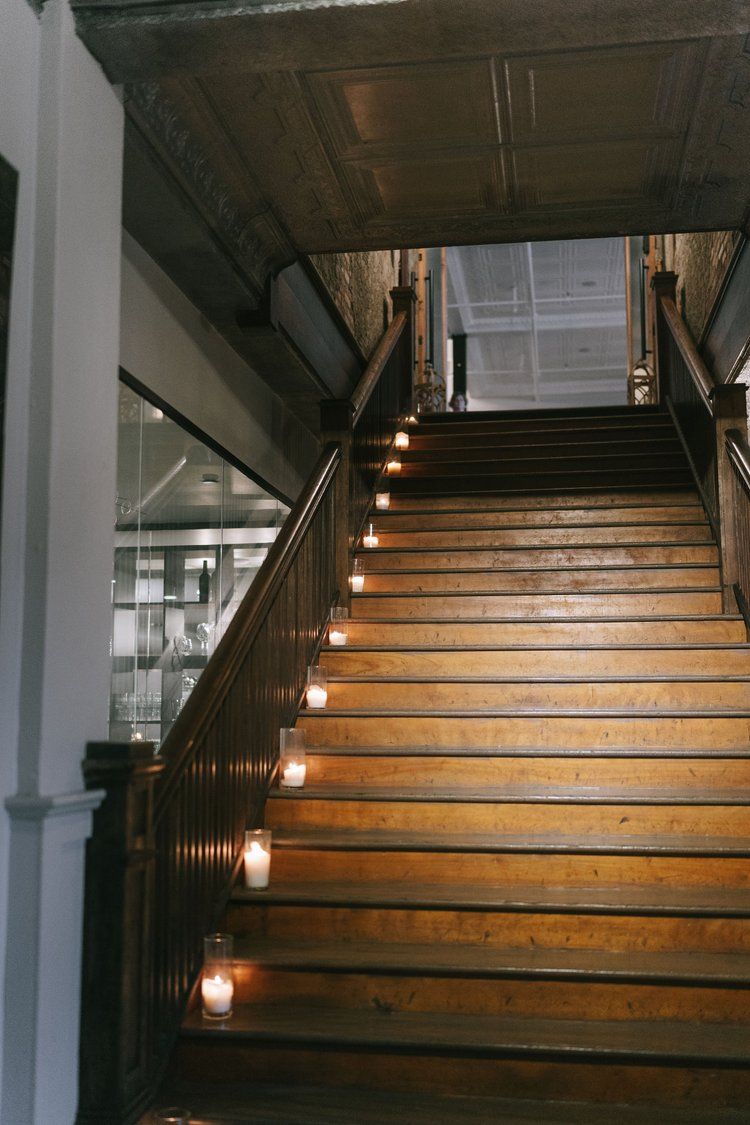Wooden staircase with candles on each step, metal railings, and ornate ceiling in elegant venue.