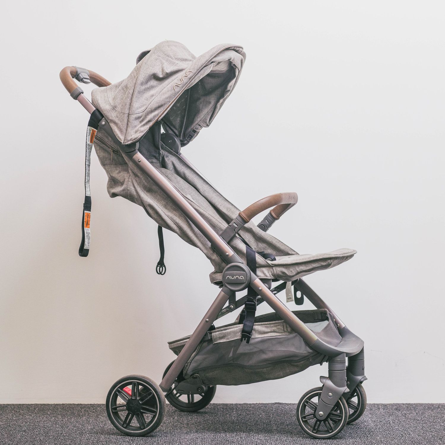 Compact gray baby stroller with canopy, brown leather handles, and red-accented wheels on a light background.