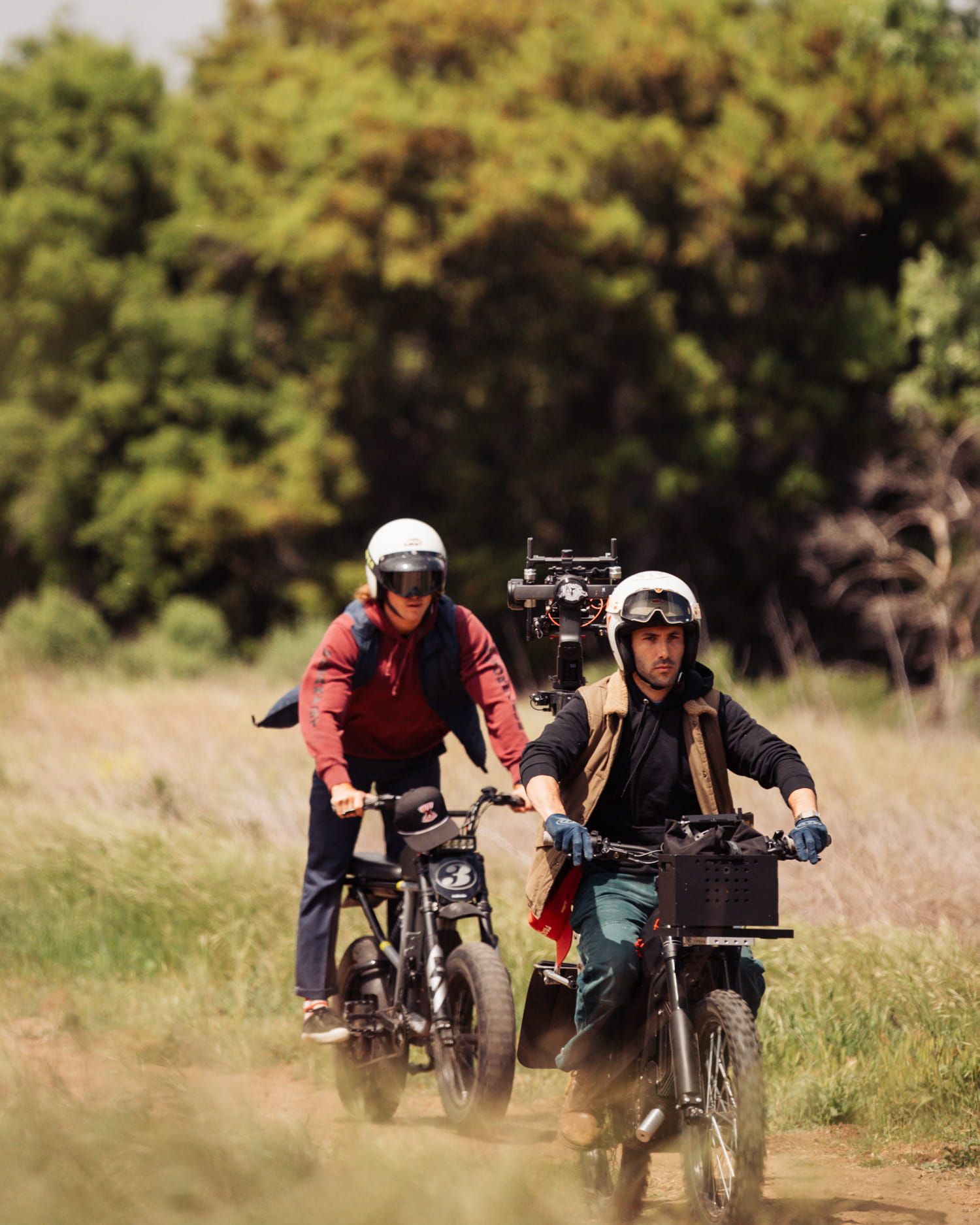 Two riders on electric bikes traverse a dirt trail through lush green wilderness.