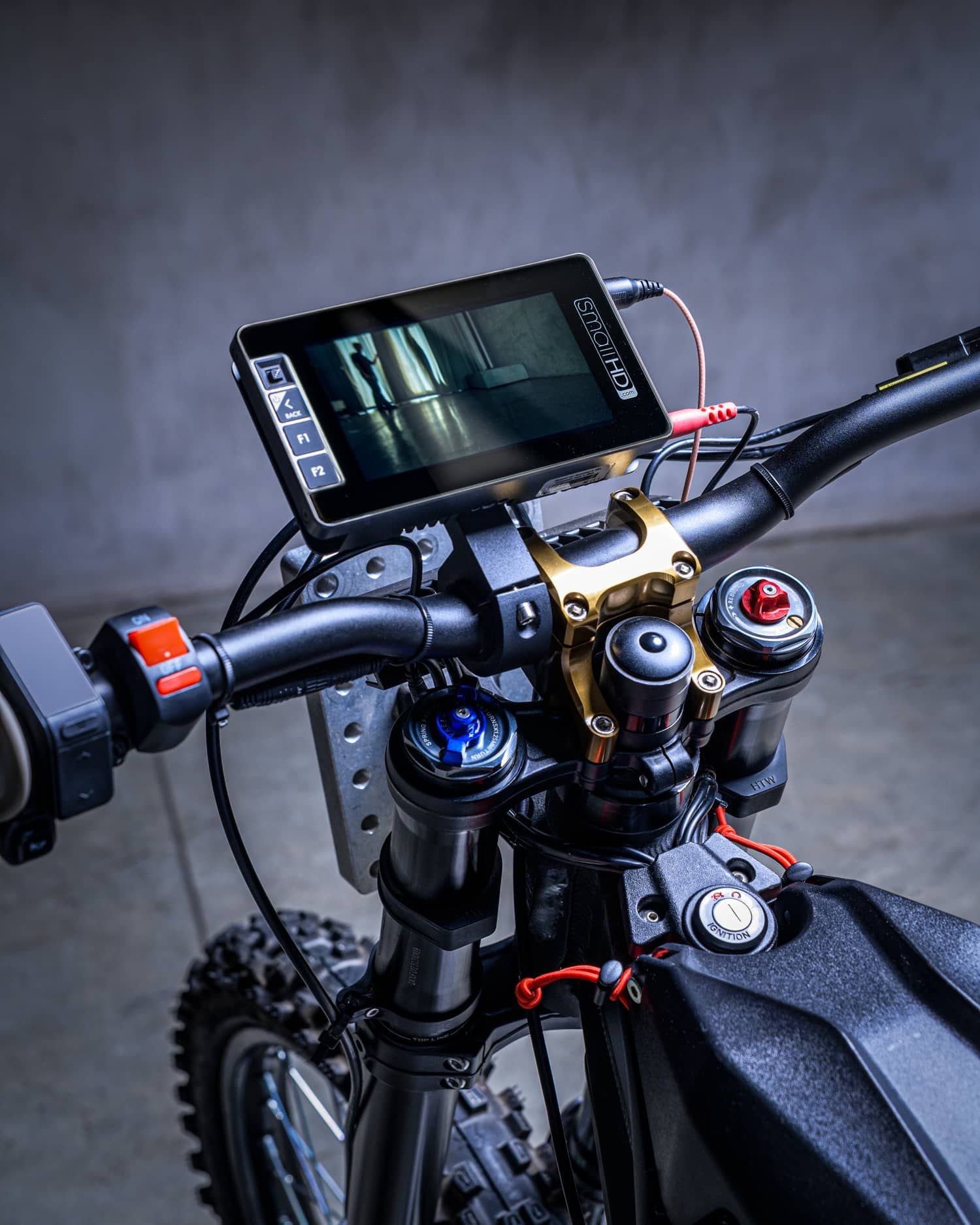Close-up of a dirt bike handlebar with a mounted digital display screen and gold stem clamp.