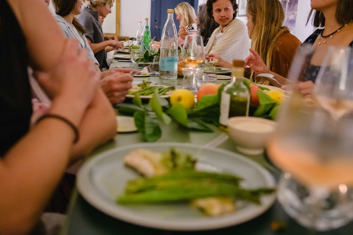 Guests gathered around a dinner table with plates of fresh vegetables, candles, and drinks at an outdoor gathering.