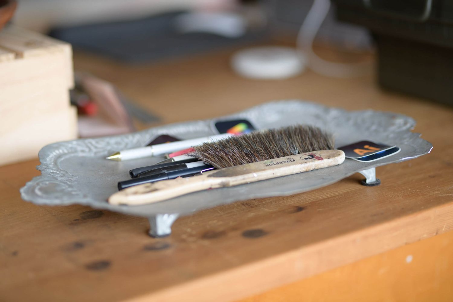 A decorative silver tray holding a brush, pencil, and credit cards on a wooden desk.