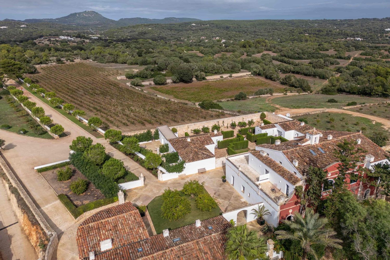 Aerial view of a Mediterranean estate with terracotta rooftops, manicured gardens, orange trees, and vineyard fields in rural Spain.