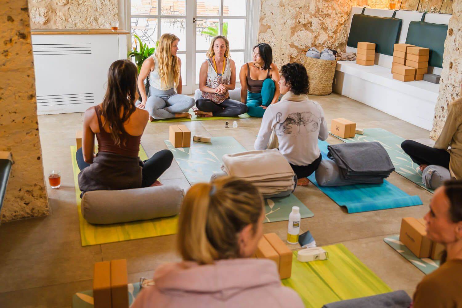 Group of women sitting in a circle on yoga mats during a wellness retreat session indoors.