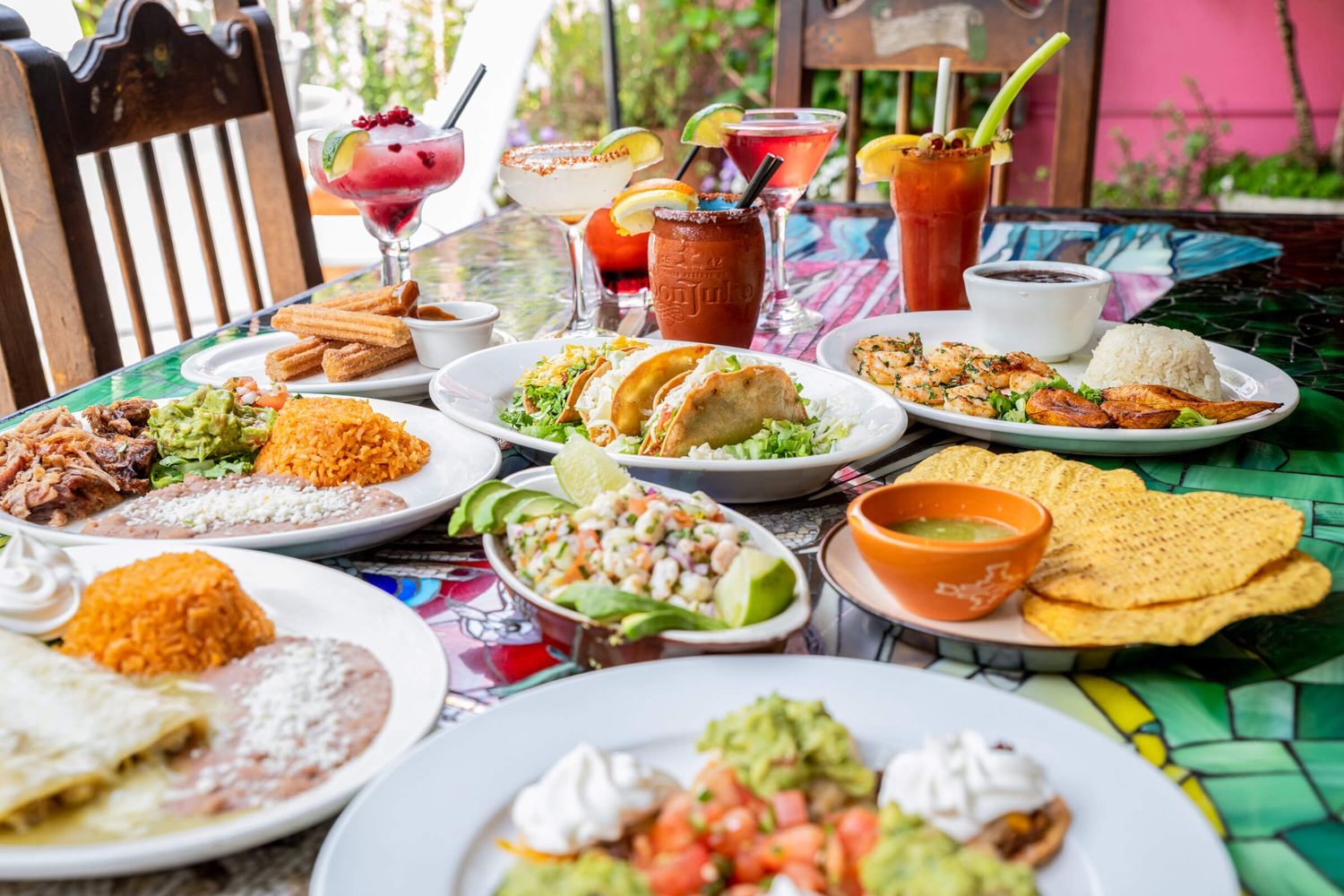 Colorful spread of Mexican dishes including tacos, guacamole, rice, beans, and vibrant cocktails on a festive table.