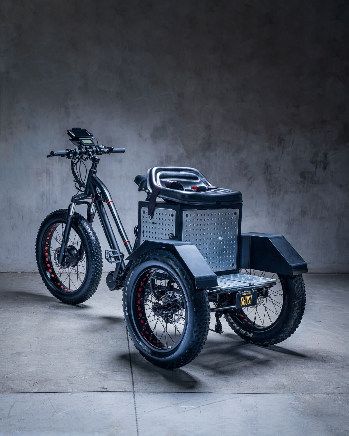 Electric camera support and stabilizer tricycle with fat tires, storage box, and rugged design parked indoors on concrete floor.