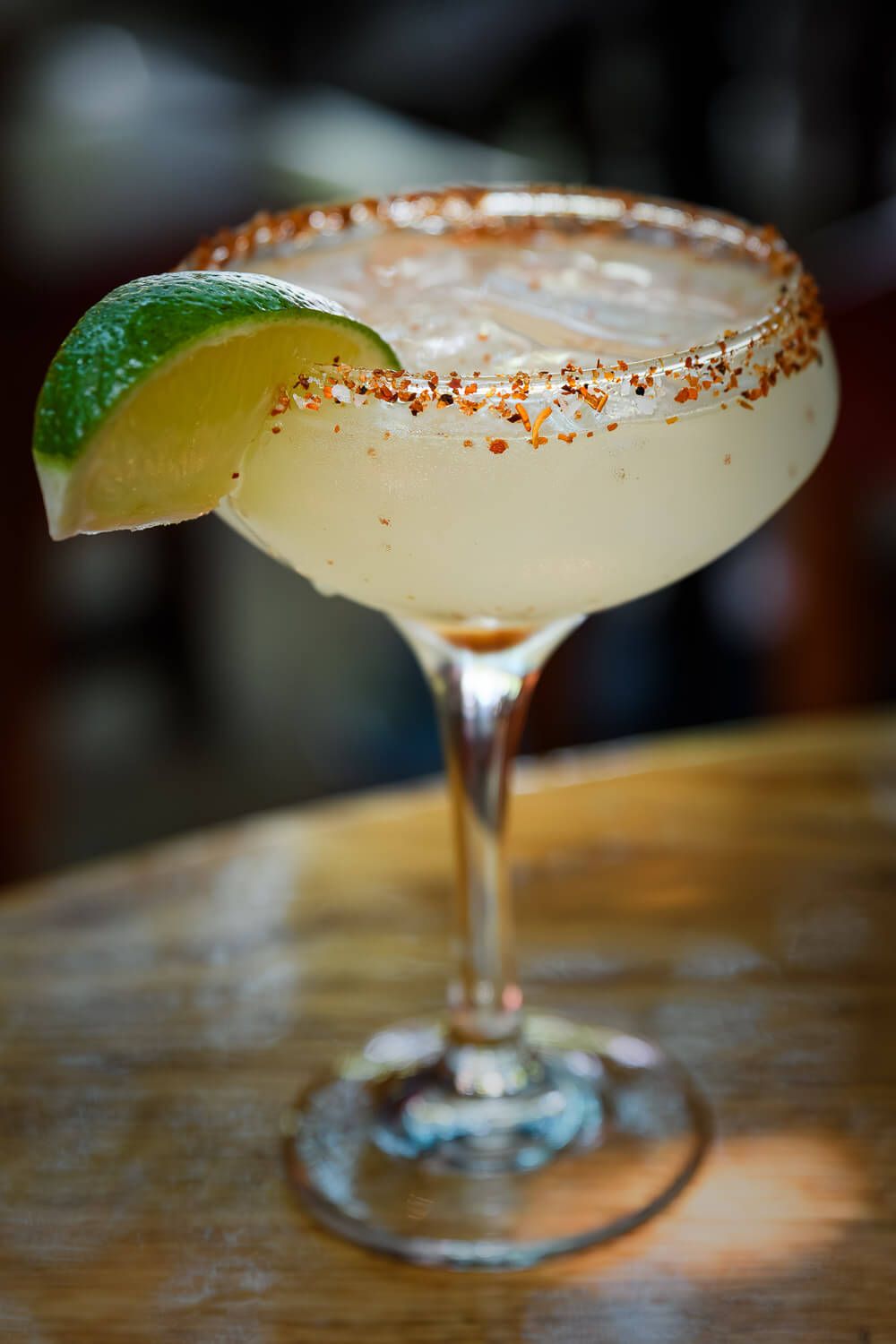 A chilled margarita cocktail in a salted rim glass garnished with a fresh lime wedge on a wooden bar.