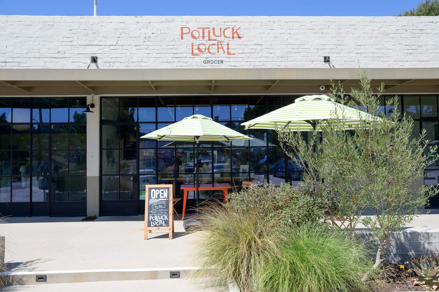 Potluck Local restaurant exterior with green patio umbrellas and outdoor seating area.