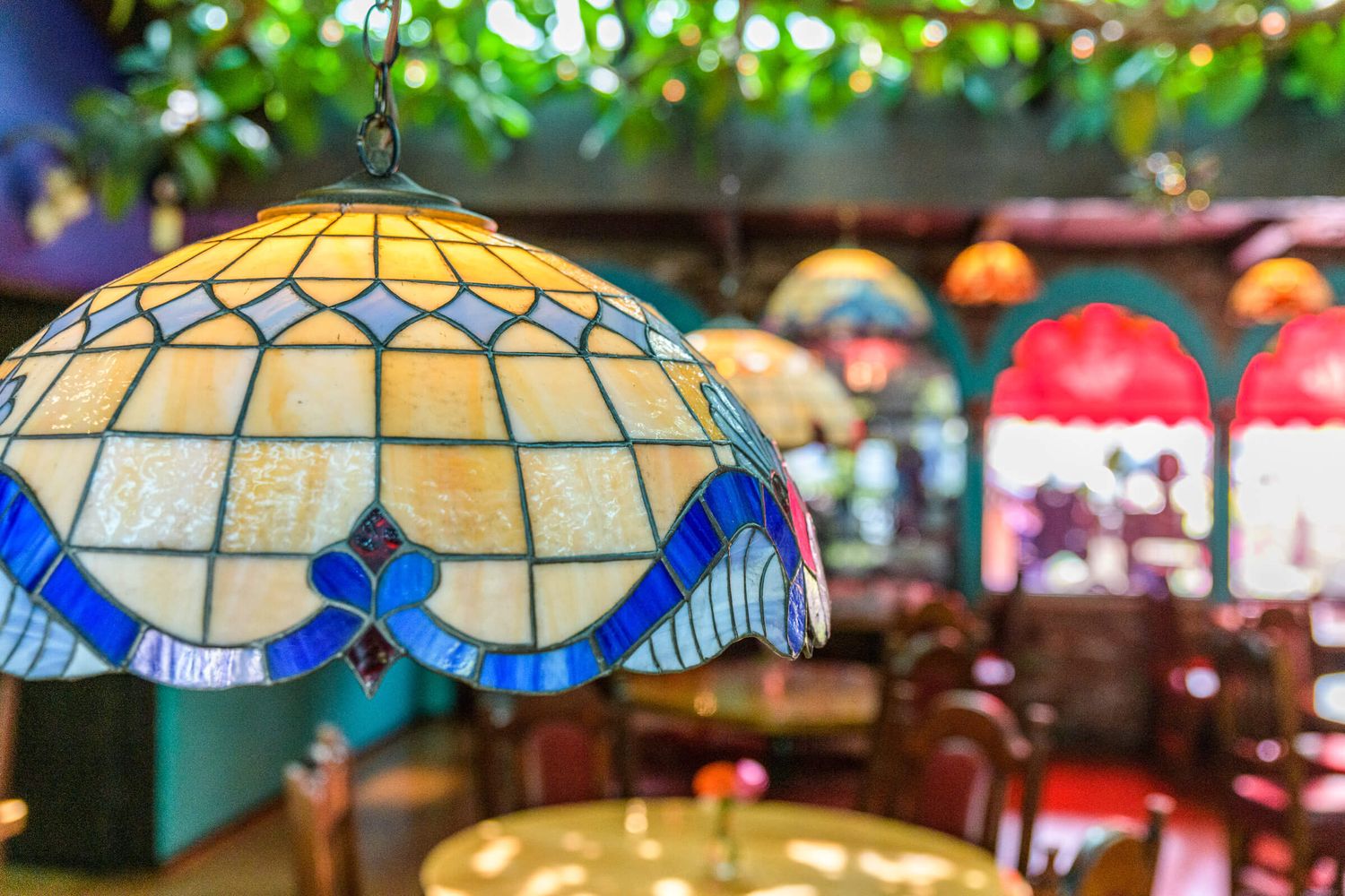 Colorful Tiffany stained glass pendant lamp hanging in a vibrant Mexican restaurant with wooden furniture.
