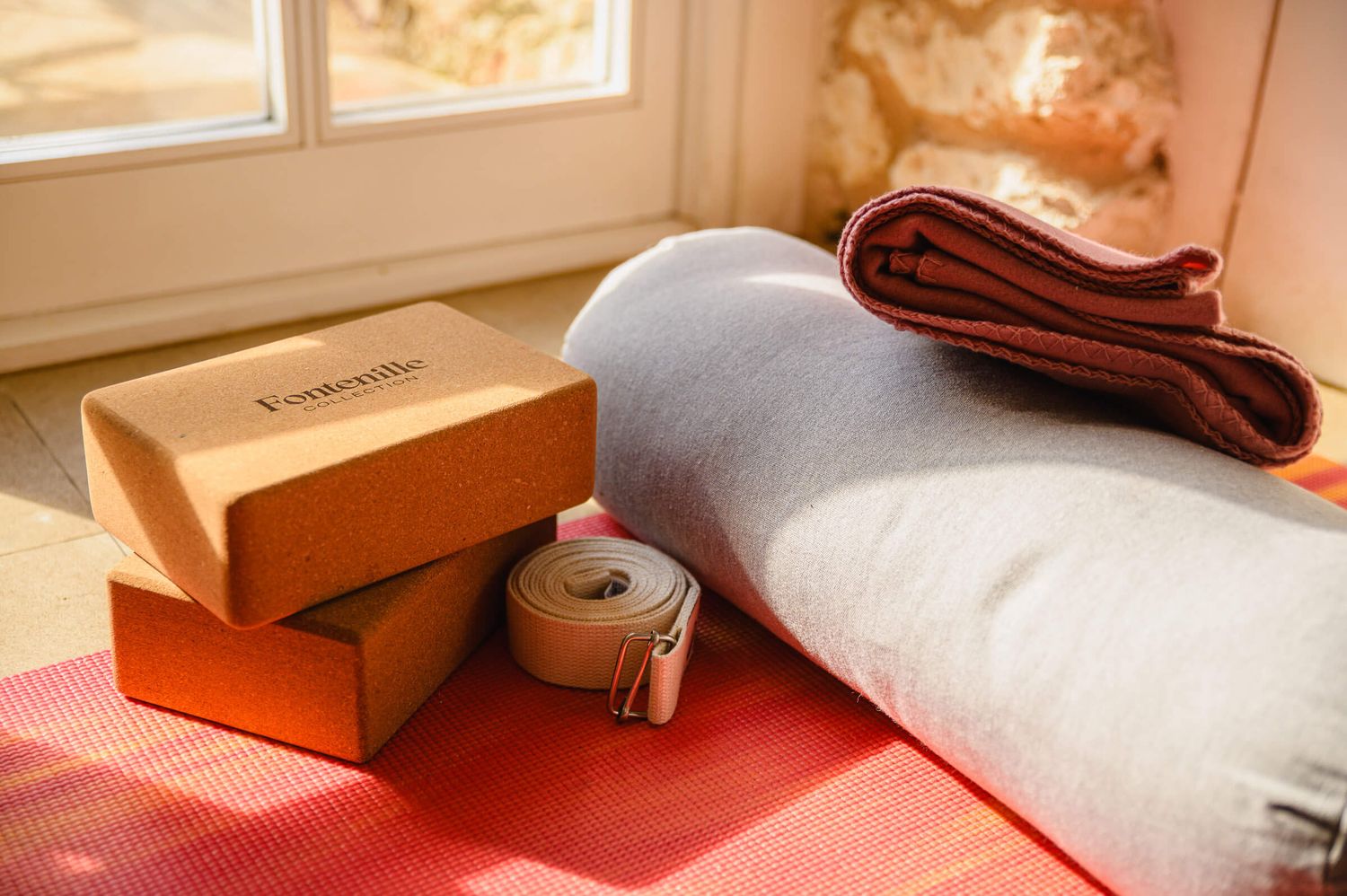 Yoga blocks, a strap, and rolled mat on a sunlit wooden floor for a yoga session.