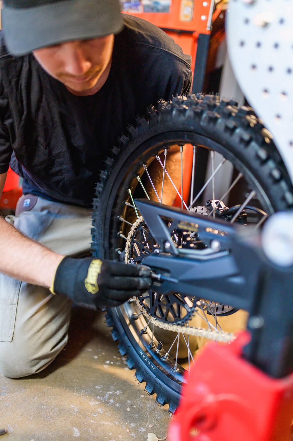 Mechanic in black gloves working on a dirt bike wheel with knobby tires in a workshop garage.