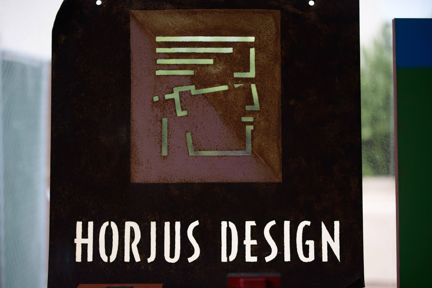 Close-up of a Horjus Design sign featuring a decorative geometric logo on a dark background.