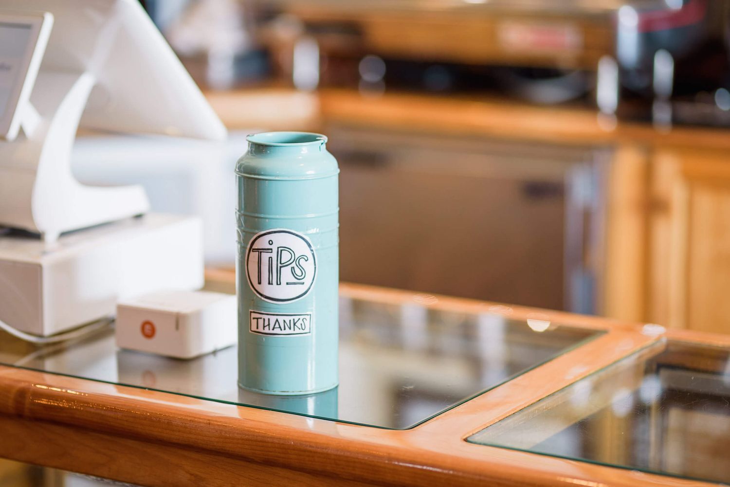 A mint green tips jar on a glass counter in a cafe or restaurant setting.