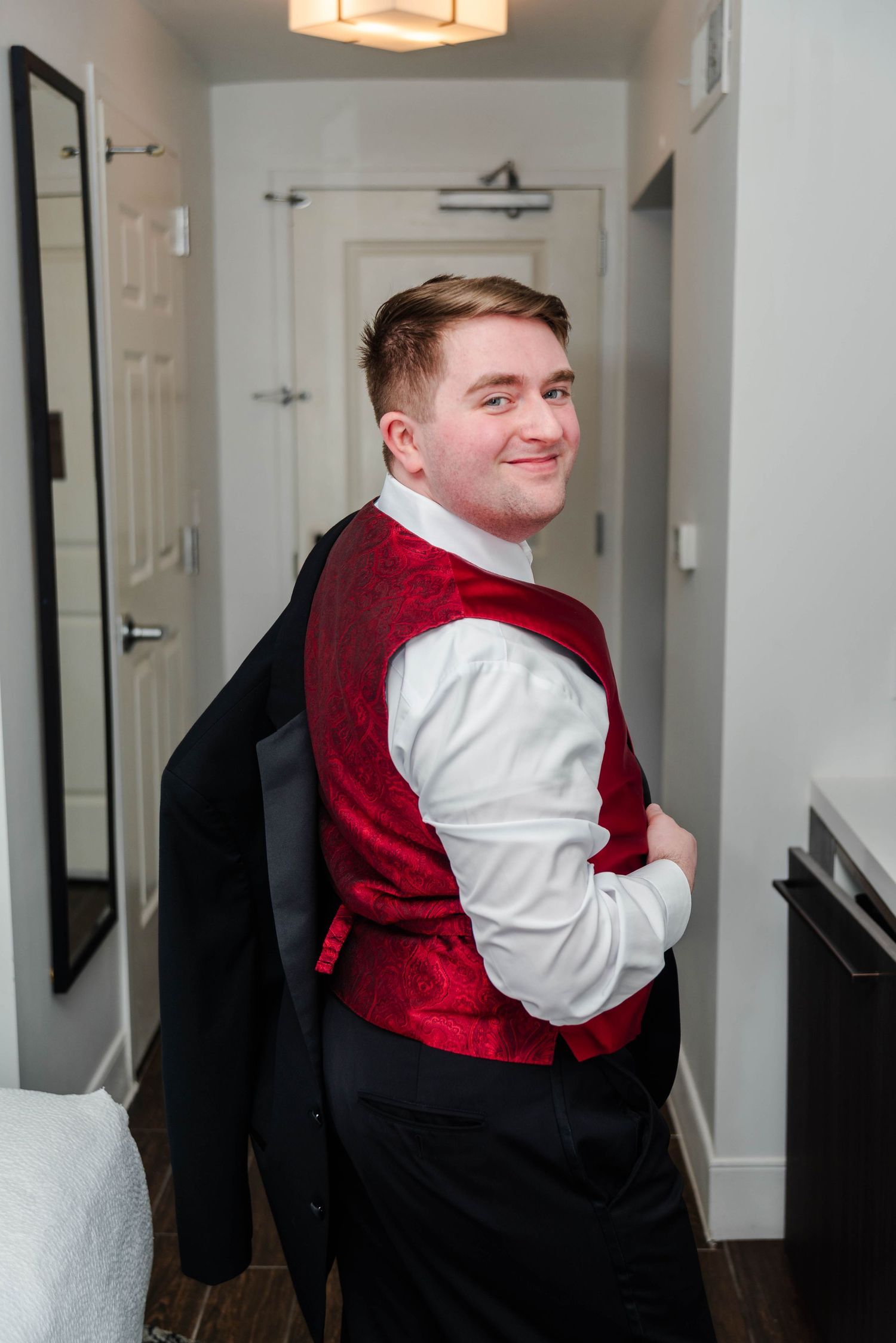 A man in a red vest posing in a hotel room.