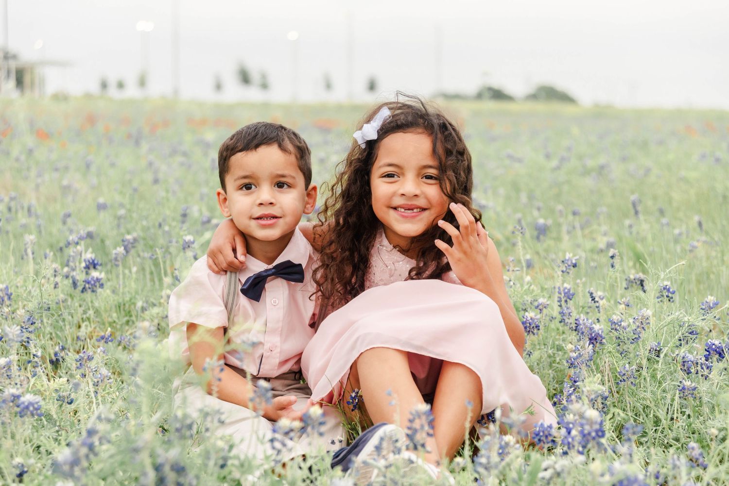 A pair of children sit together smiling in bluebonnets